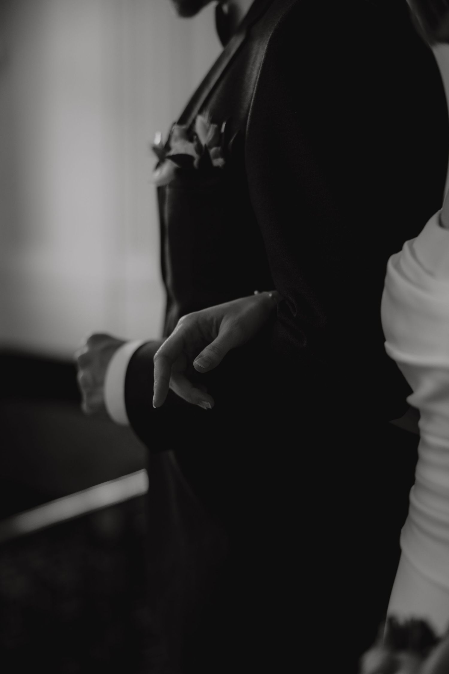Close-up detail of groom's formal black suit jacket and white shirt cuff.