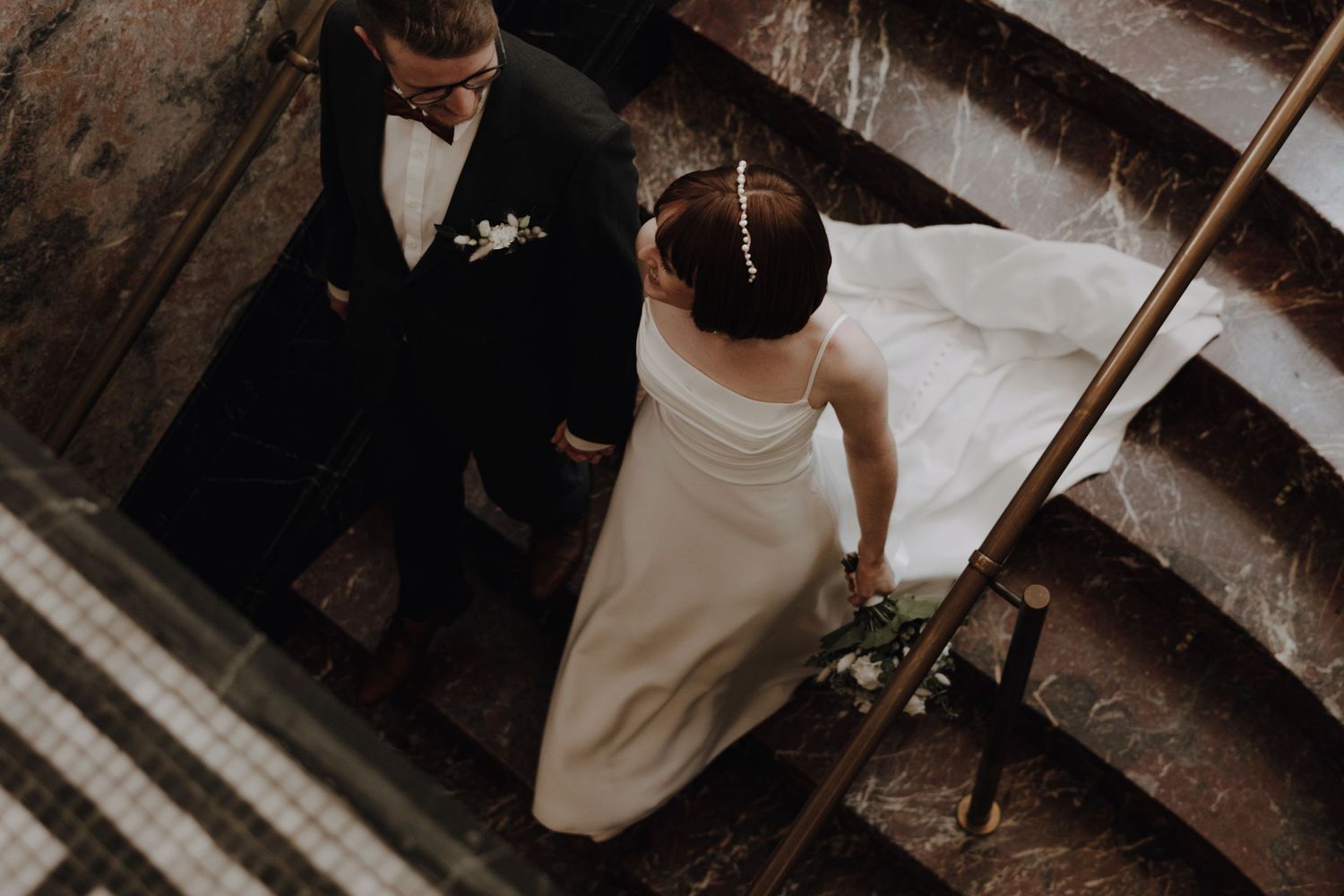 Newlyweds walking down decorative stairs in classic wedding attire.