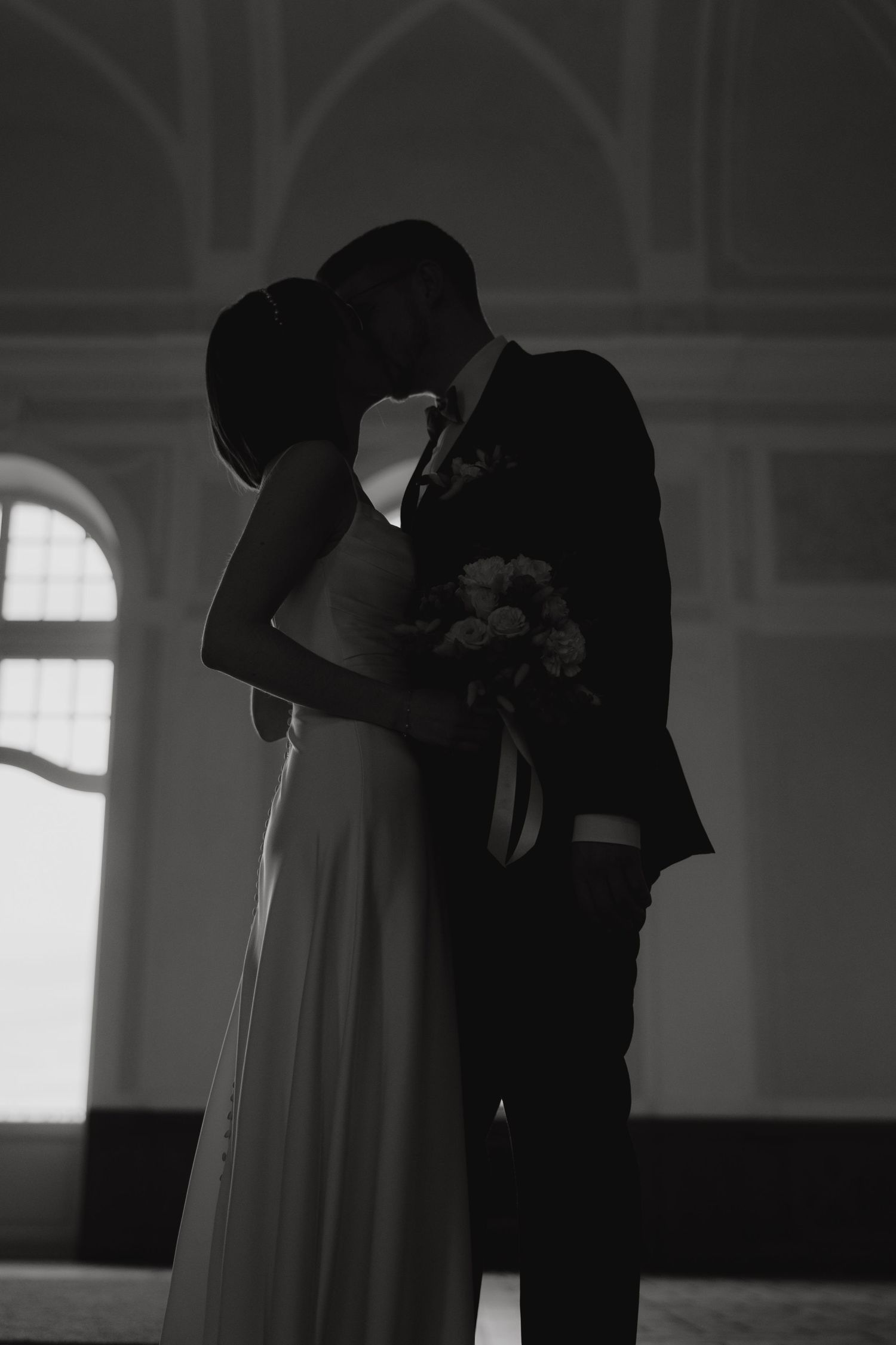 Romantic black and white silhouette of couple sharing intimate moment by arched windows.