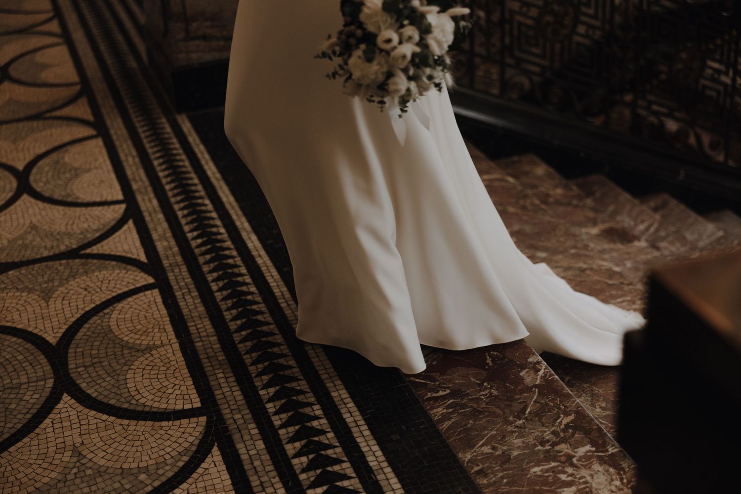 Detail shot of bride's flowing white gown against ornate patterned carpet.