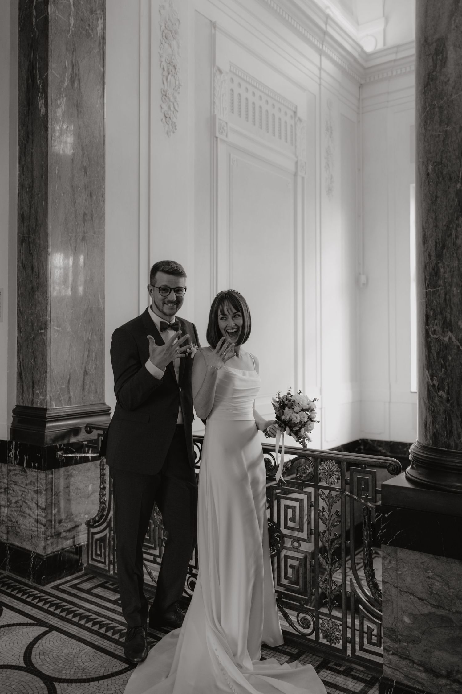 Wedding couple poses together on marble floor with elegant architectural details.