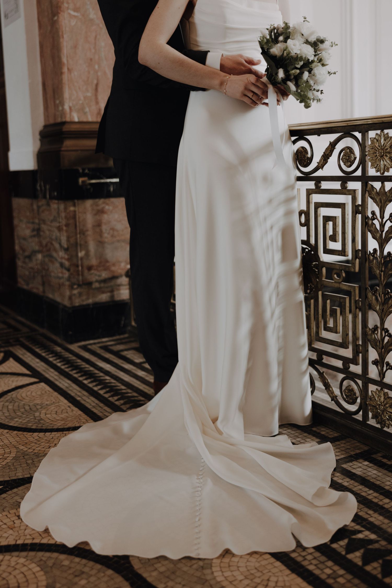 A wedding couple poses elegantly on a decorative tiled floor with ornate railings in the background.
