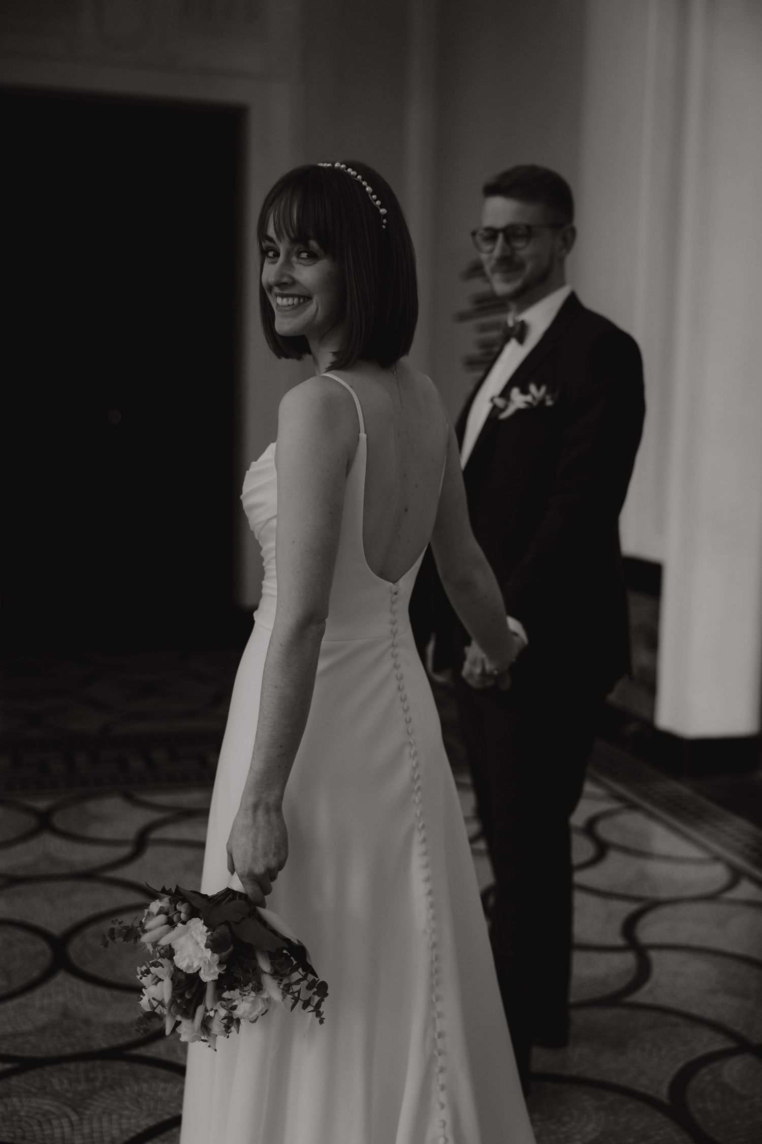 Wedding couple stands together on ornate floor showing detailed back of elegant white dress.