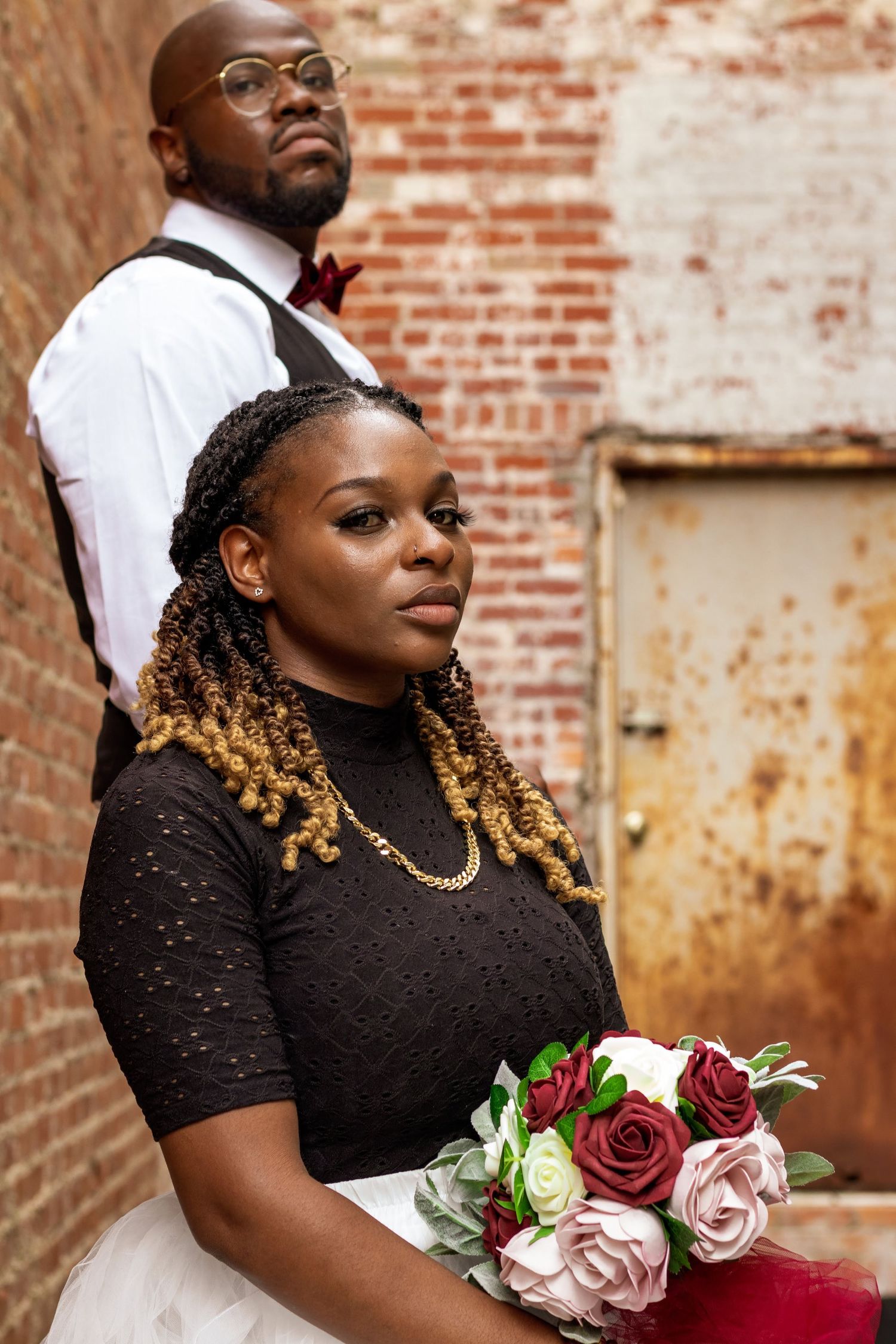 Wedding portrait against rustic brick wall with red and pink rose bouquet.