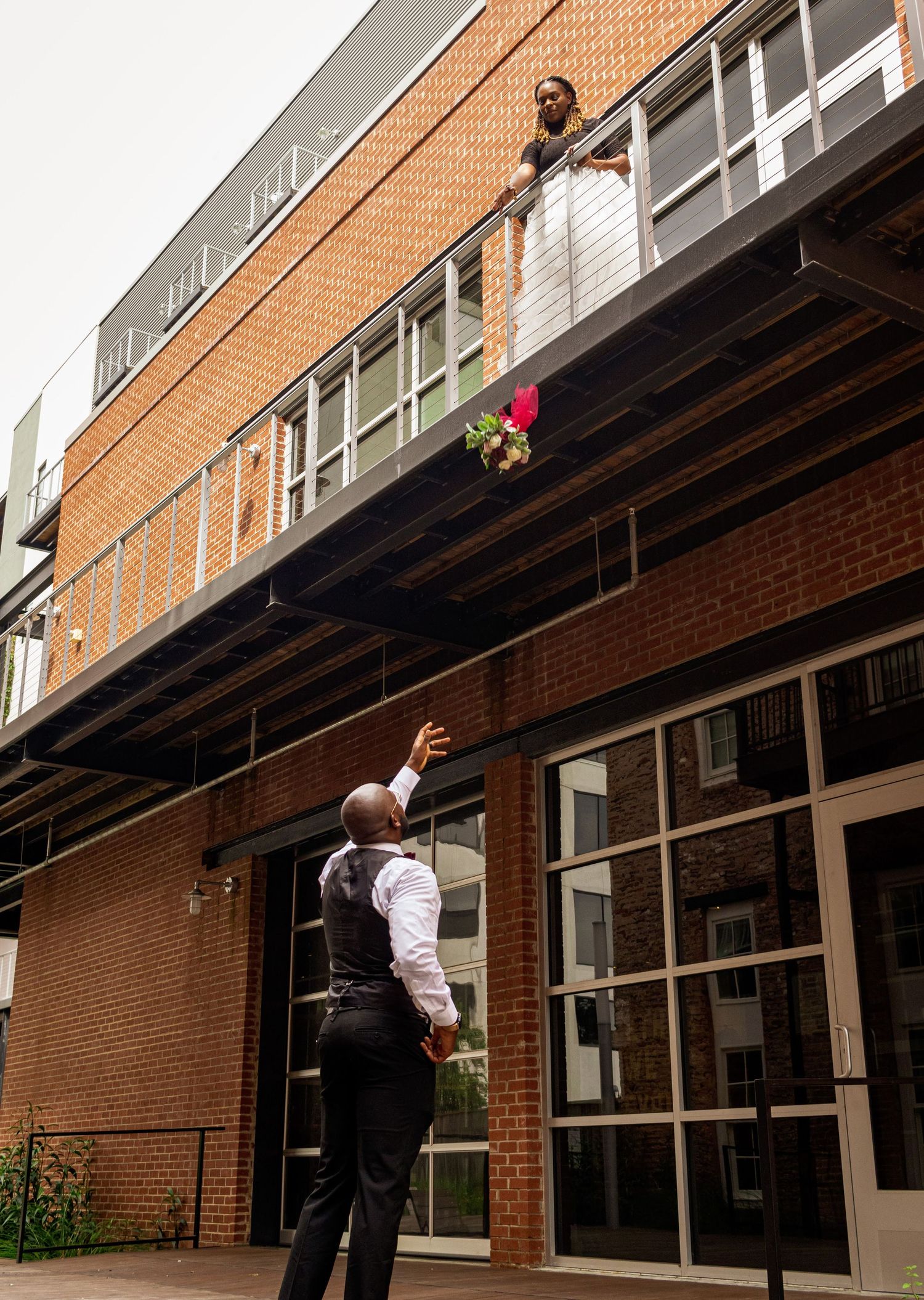 Fun wedding photo with someone tossing a bouquet from a balcony.