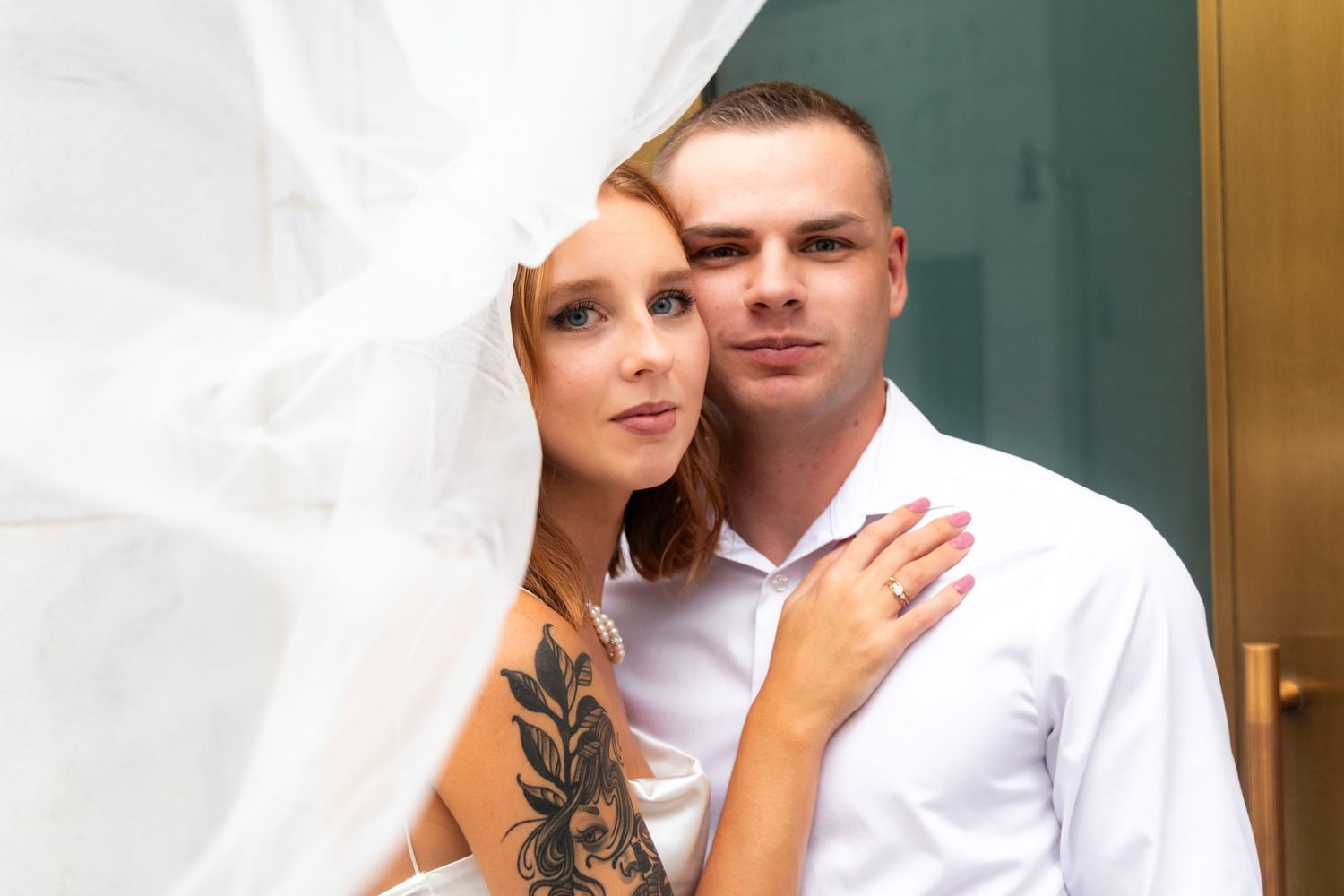 Romantic portrait of couple under flowing veil against green door.