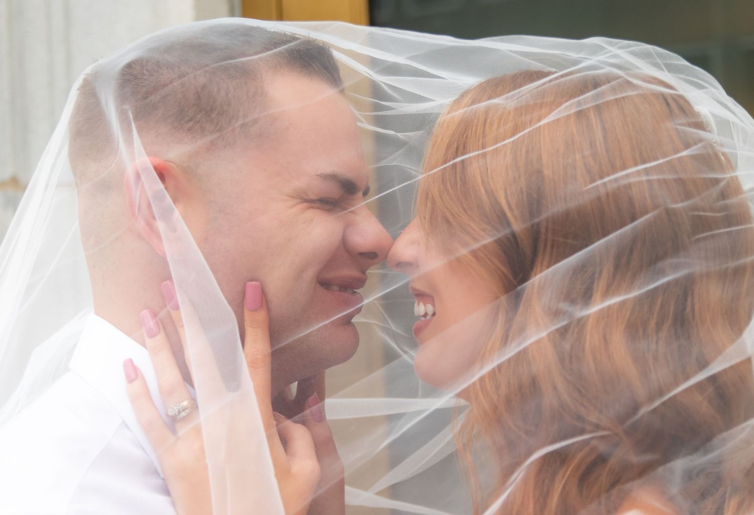 Intimate moment between couple beneath sheer wedding veil.