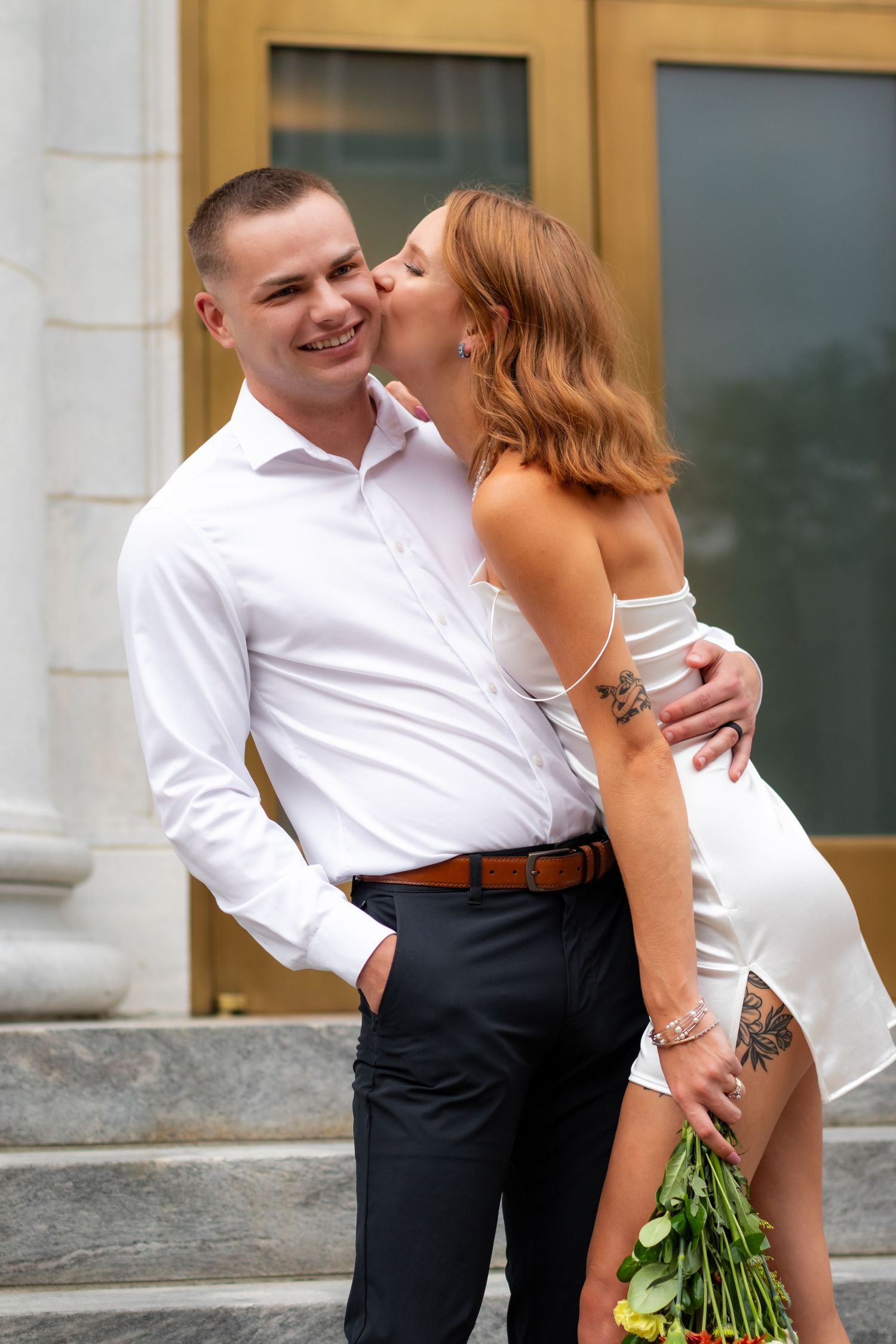 A romantic couple shares a tender moment on stone steps, with her wearing white and him in formal attire.