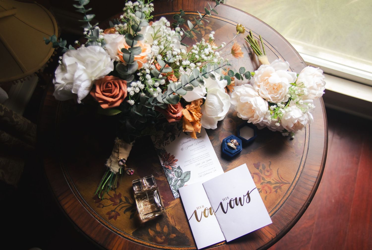 Flat lay photo of bride's bouquet, vow books, and perfume.