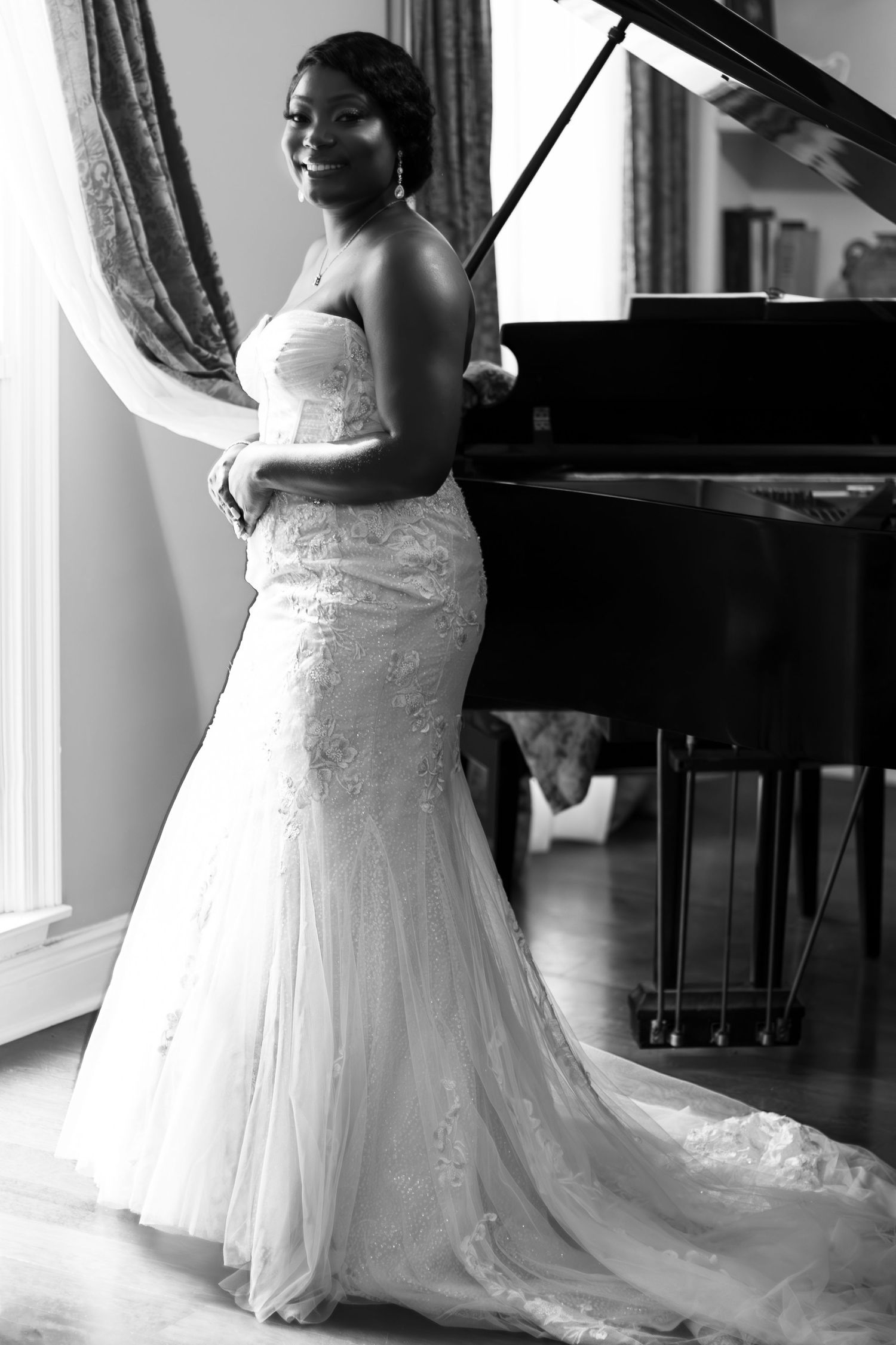 Black and white photo of bride standing next to a grand piano.