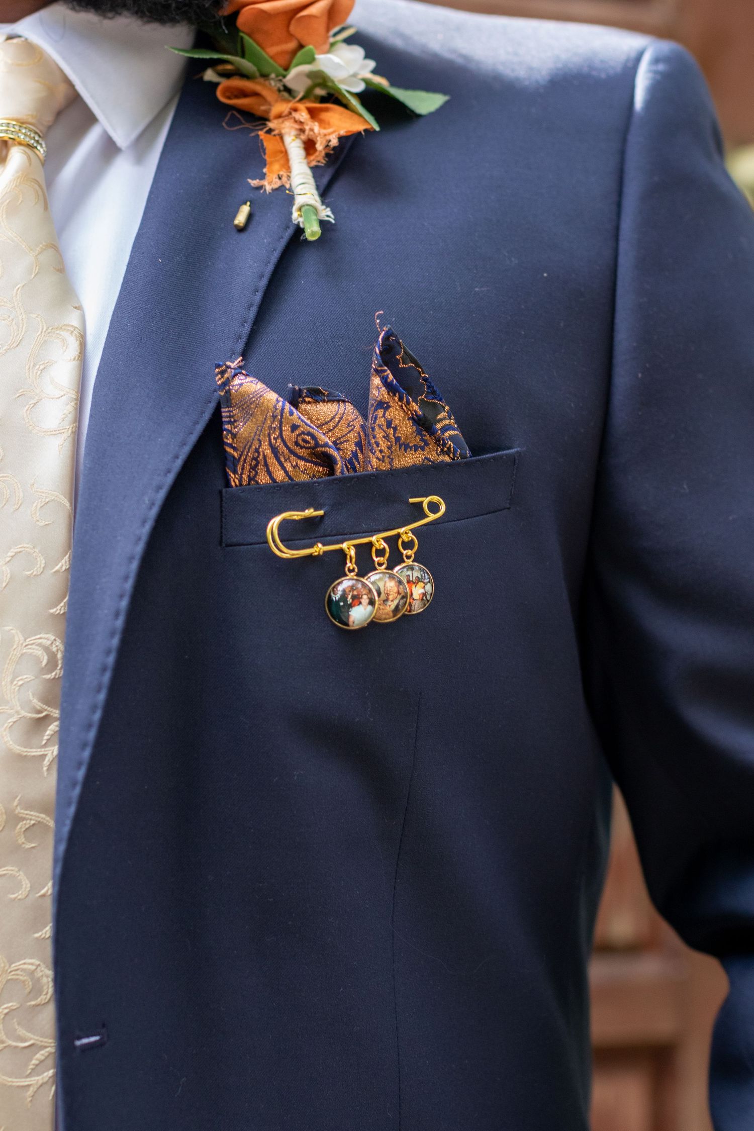 Navy blue suit jacket with orange boutonniere and decorative pocket square pin.