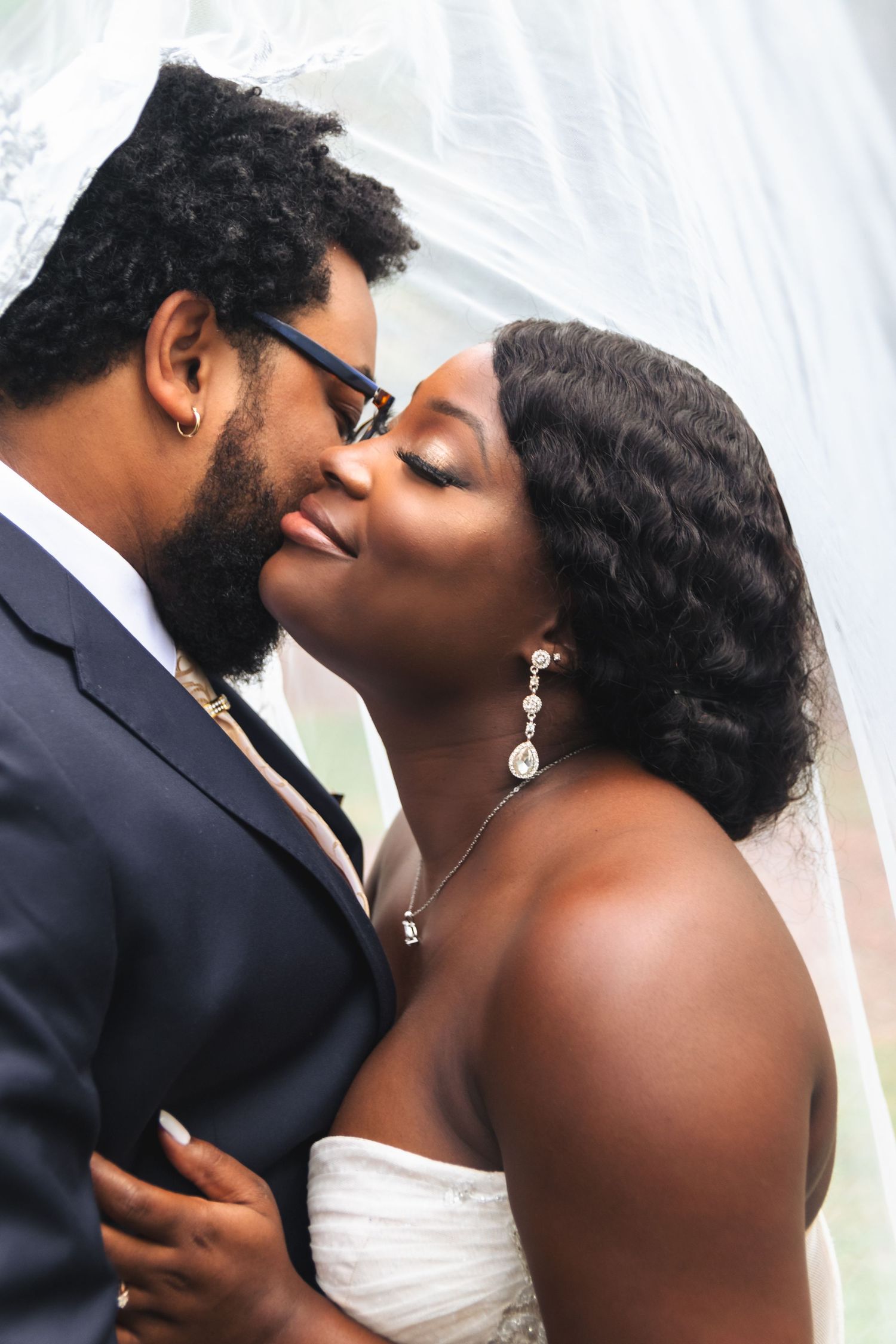 Close-up of tender moment between newlyweds under a wedding veil.