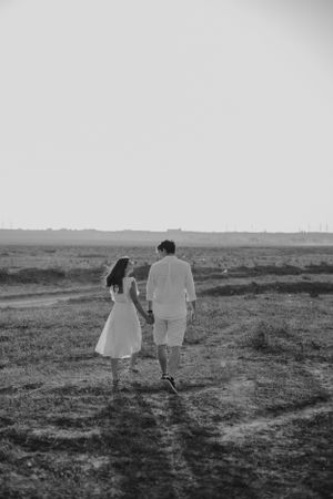 Monochrome image of two people walking together across an open field at dusk.