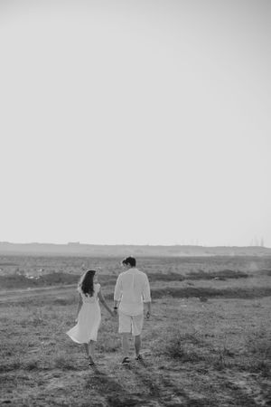 Black and white photo of a couple walking together across a rural landscape.