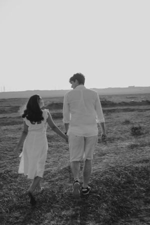 A couple holding hands while walking through a scenic field at sunset.