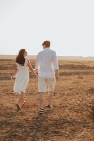 Couple in matching white outfits walking together across a sun-lit field.