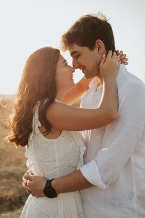 Romantic couple in white outfits embrace during golden hour in a desert landscape.