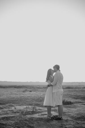 Black and white photo of a romantic embrace on a windswept field at sunset.