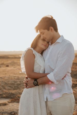 Intimate moment between couple in white clothing against desert backdrop at sunset.