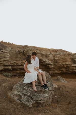 Couple sits together on rocky outcrop during outdoor photo session.