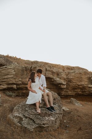 Couple sharing intimate moment while seated on large desert boulder.
