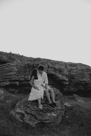 Black and white photo of couple seated on rocky formation.