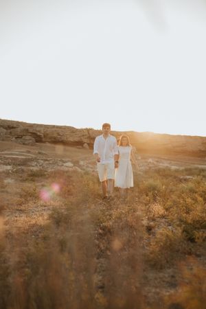 Couple in matching white outfits walking along hilltop during golden hour.