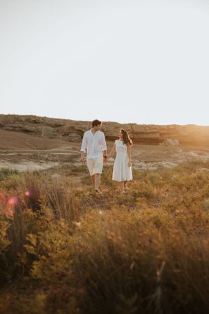Couple walking through desert brush during sunset photoshoot.