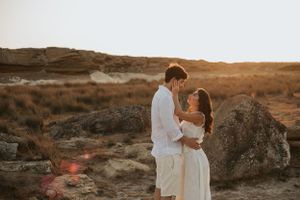 Couple in white clothing embracing against desert sunset backdrop.
