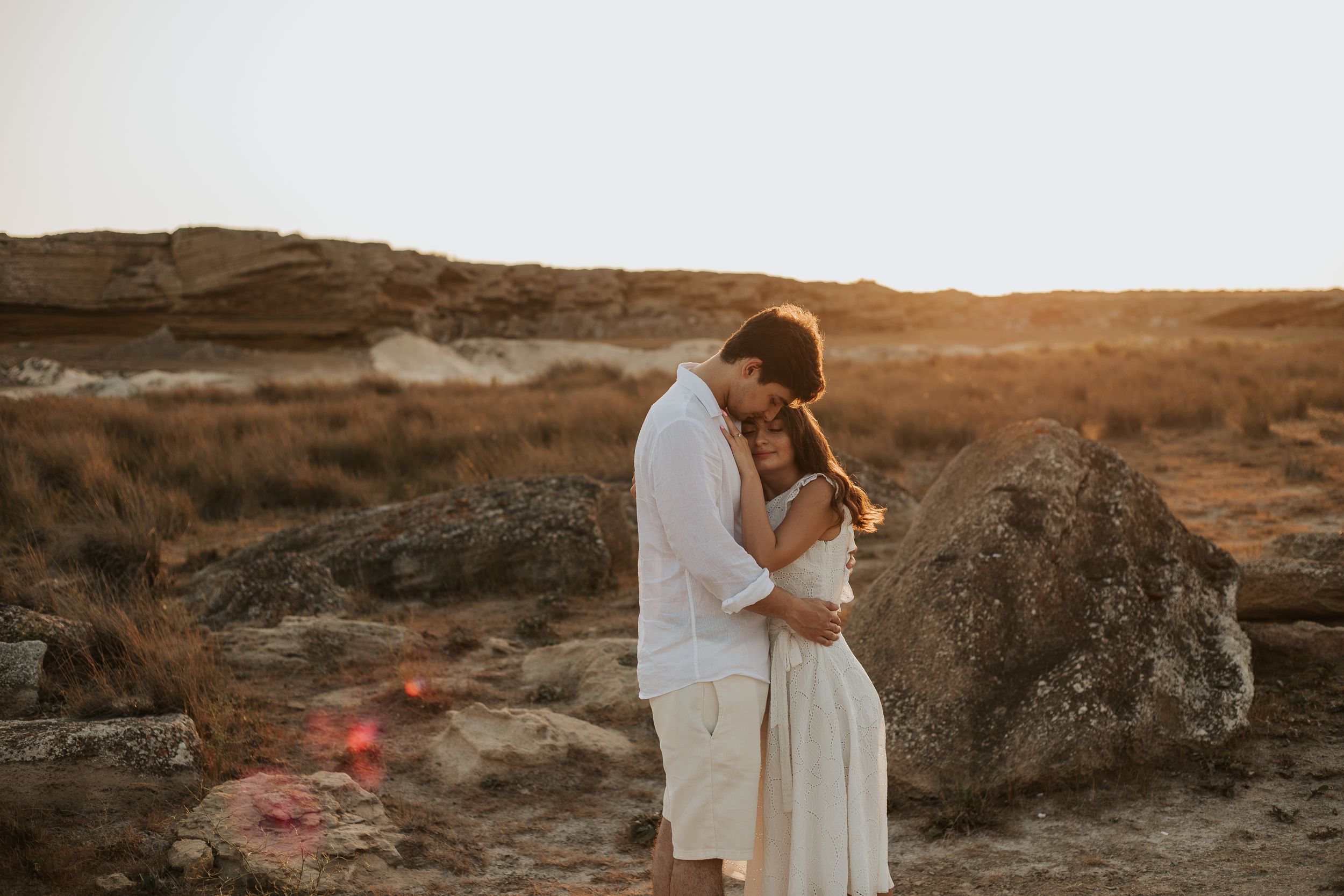A romantic sunset embrace against rocky desert terrain creates a dreamy silhouette.