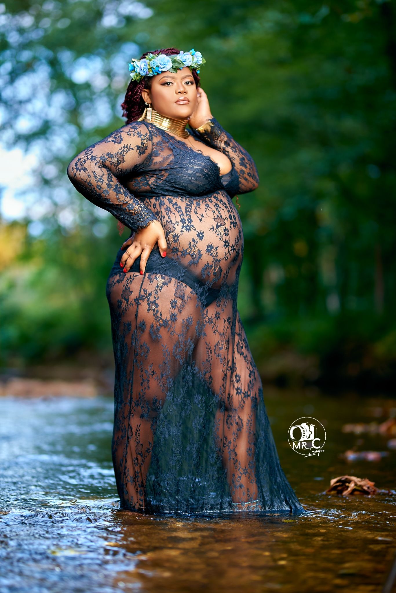 Maternity portrait in flowing lace dress standing in shallow water with floral crown.