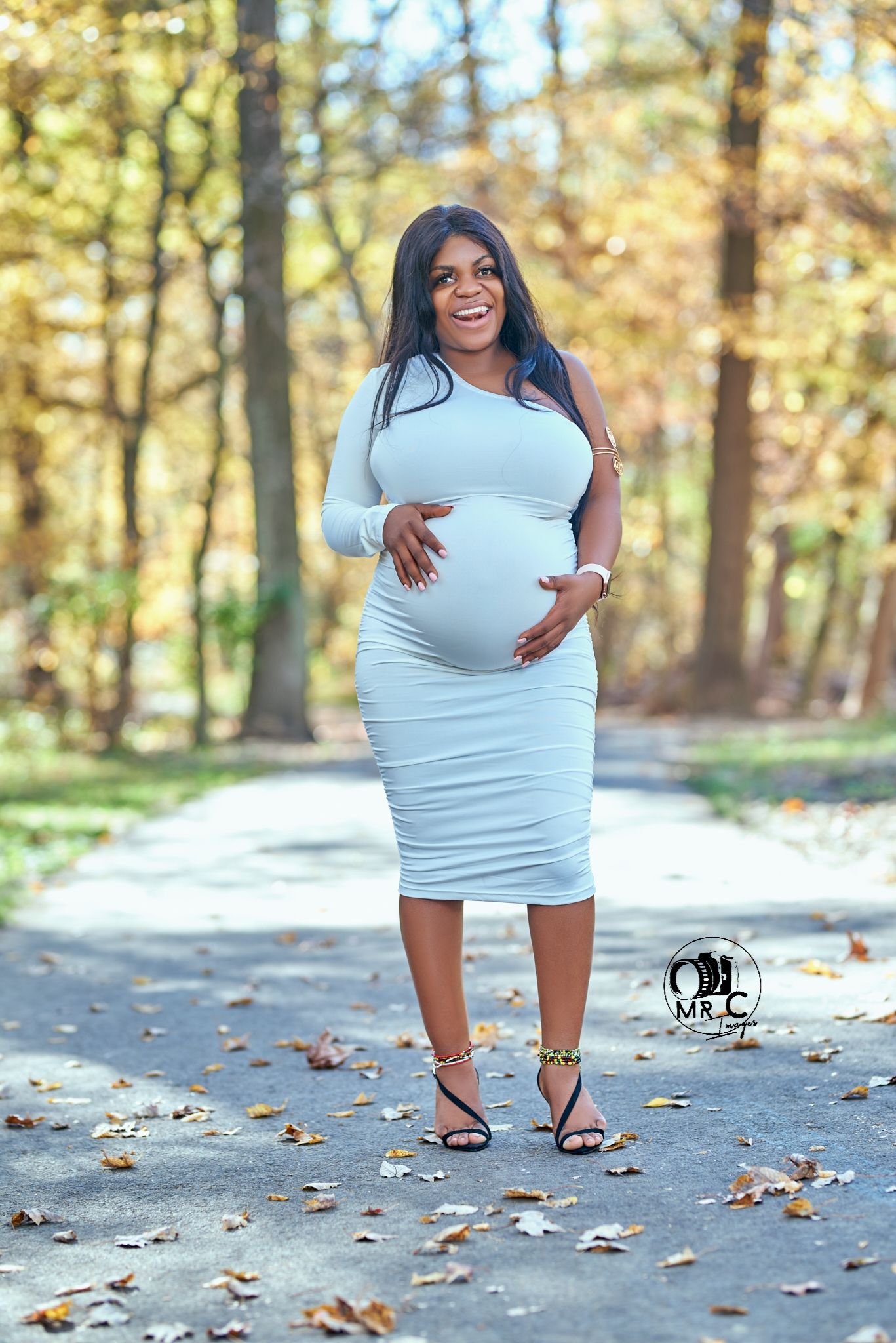 Elegant outdoor maternity photo featuring a fitted white dress and autumn forest scenery.