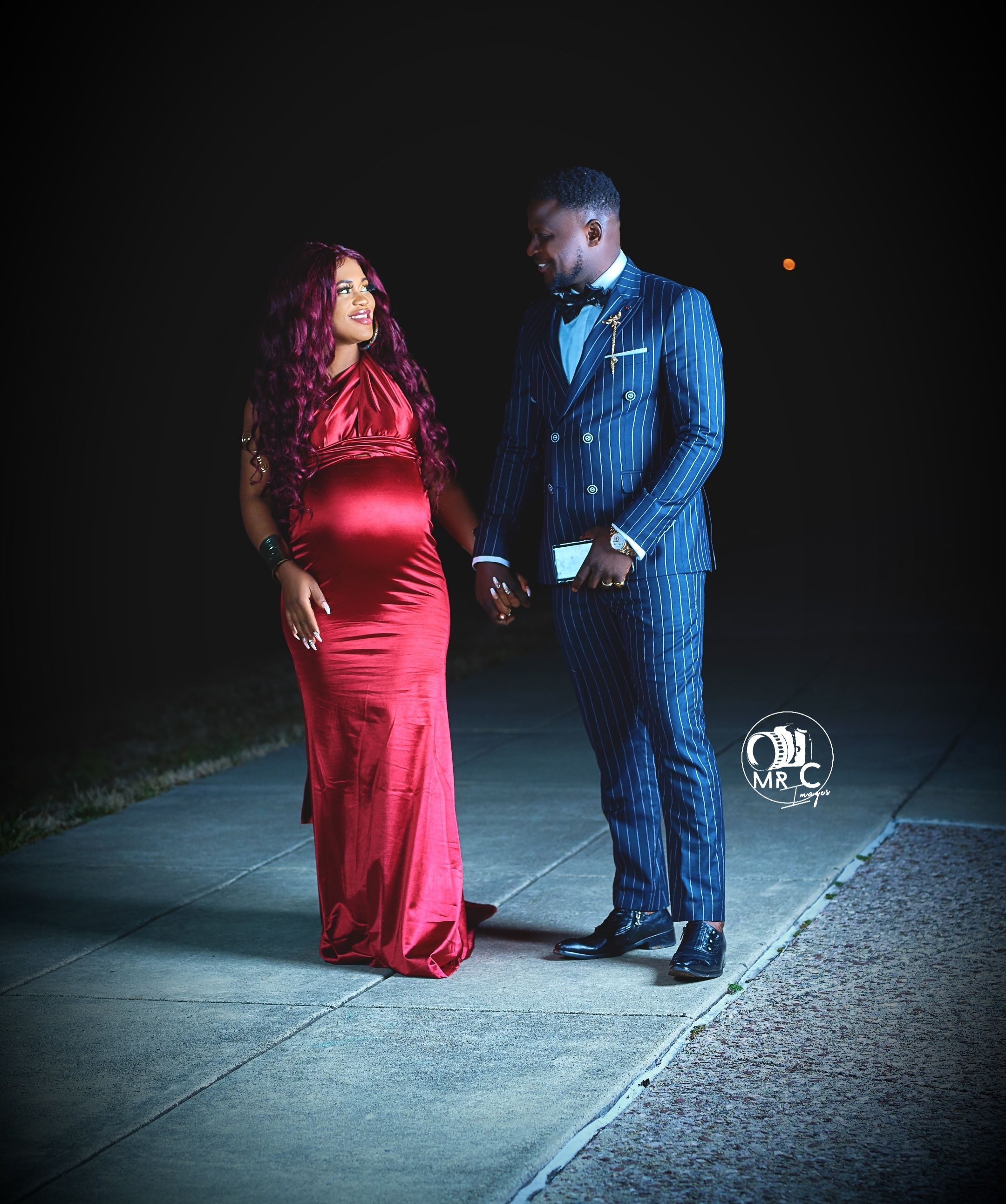 Elegant couple's portrait featuring red satin and blue pinstripe attire in dramatic nighttime lighting.