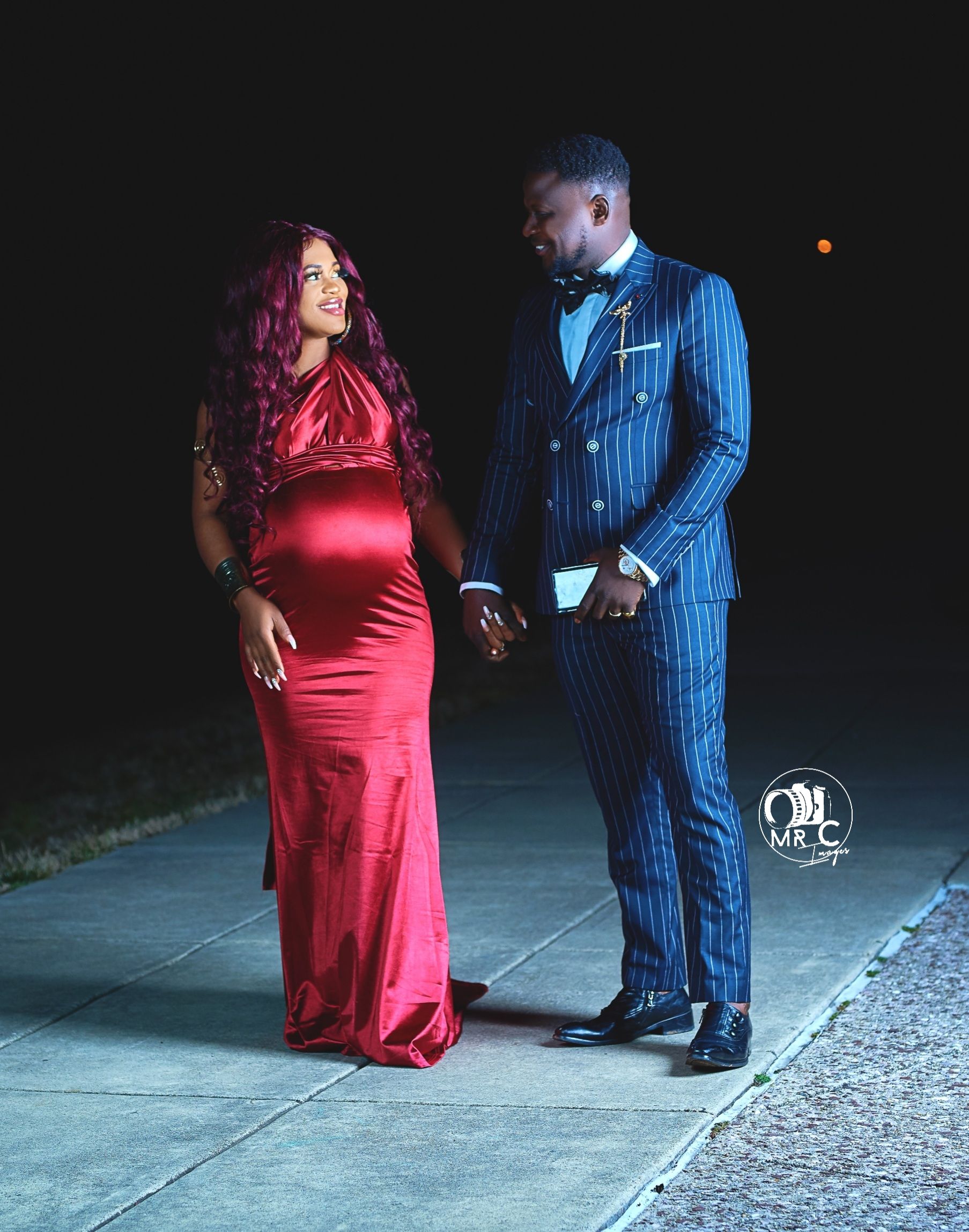 Romantic evening photo shoot with a red satin gown and blue pinstripe suit on a moonlit sidewalk.