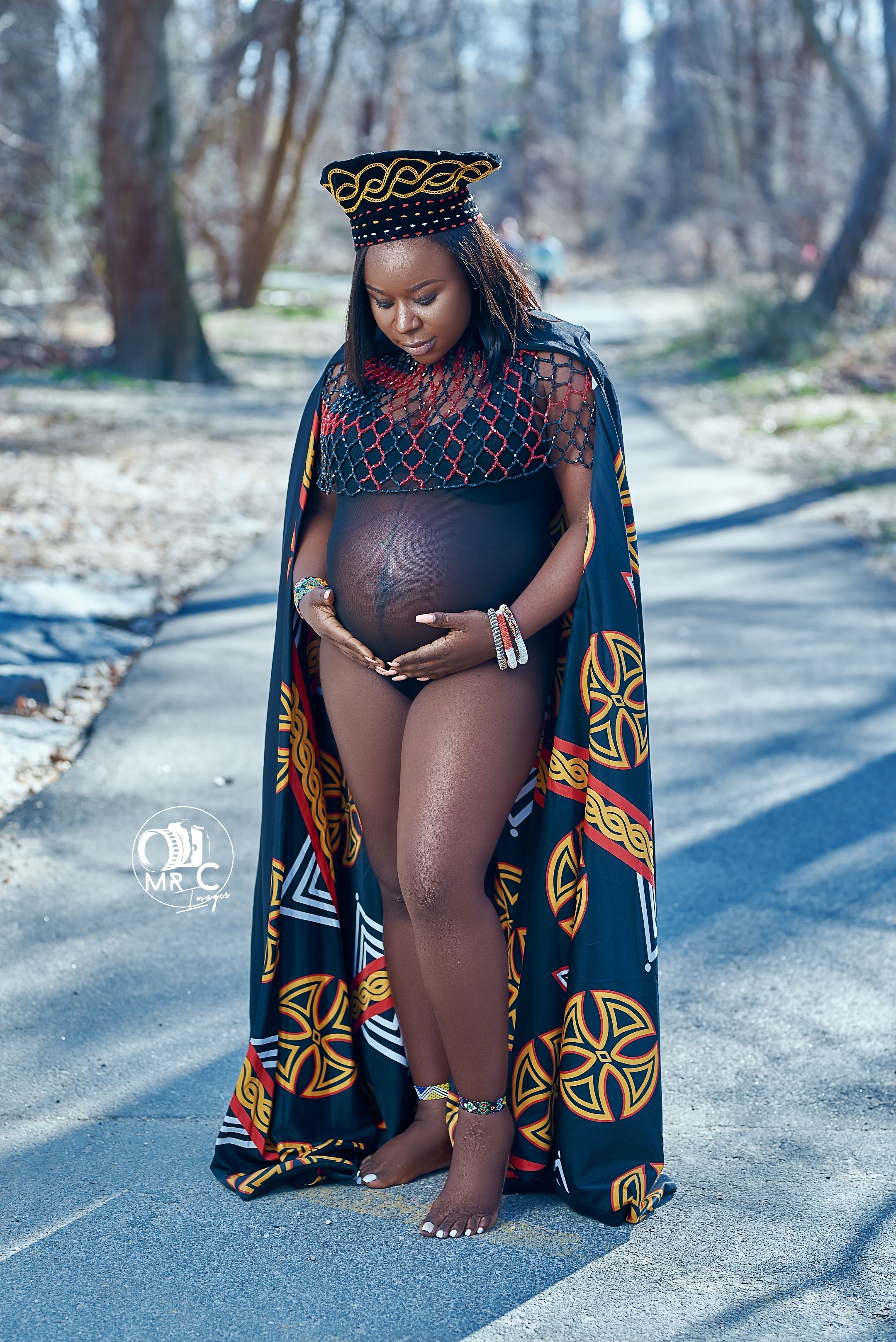 Winter maternity portrait outdoors featuring black cape with traditional African patterns.