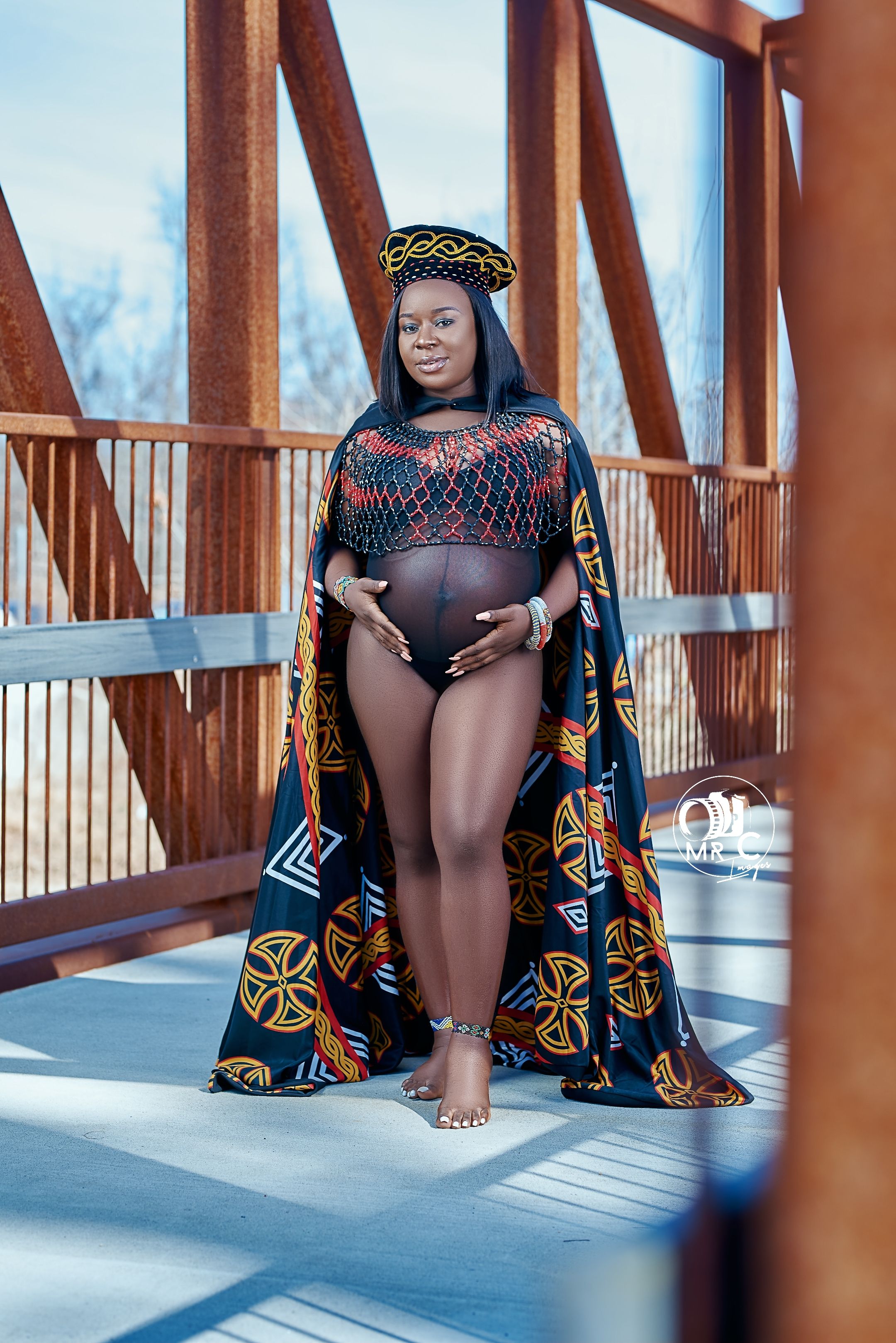 Maternity photo on bridge featuring geometric print cape and traditional African styling.