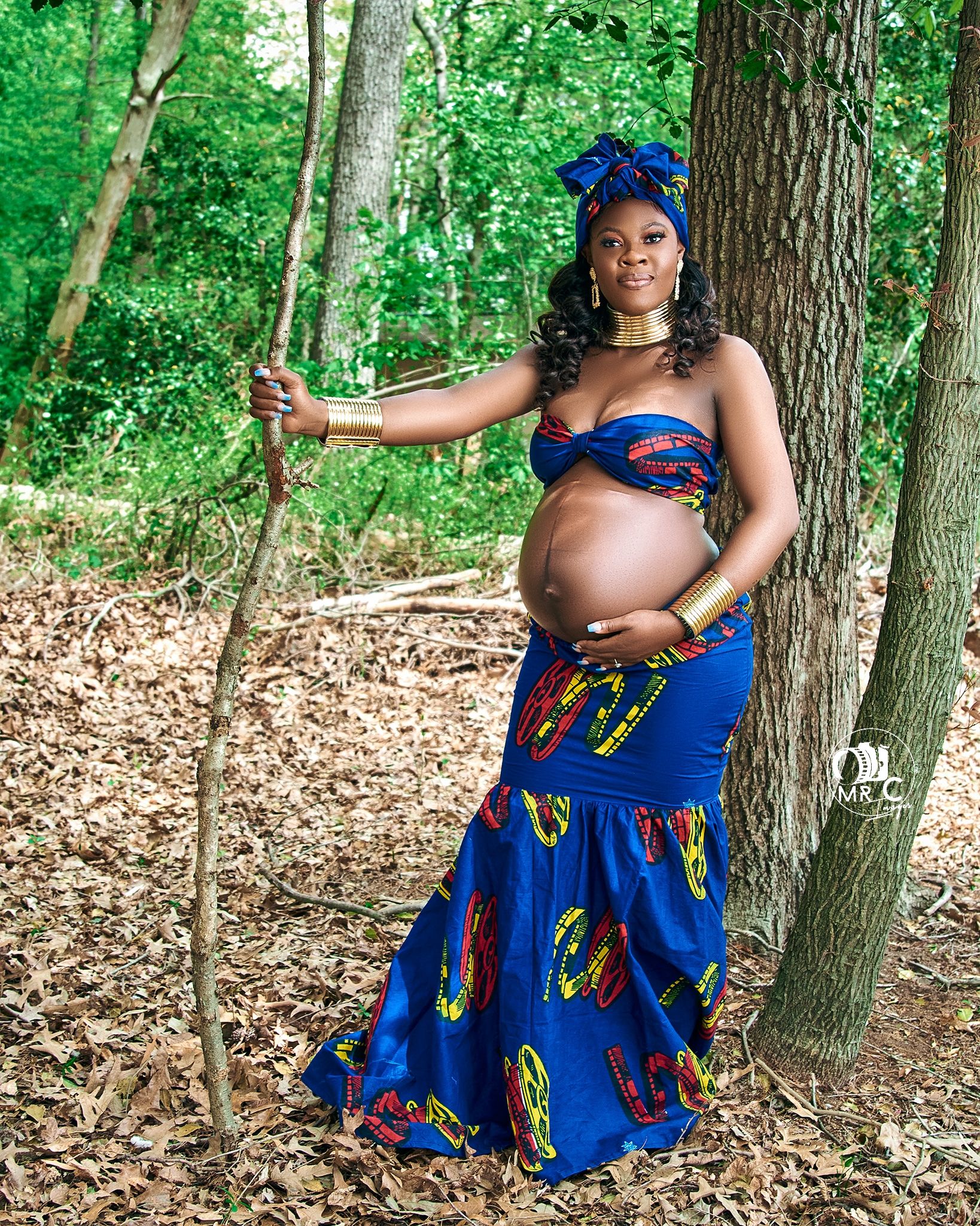 Maternity photo in forest setting with traditional blue African print dress and headwrap.