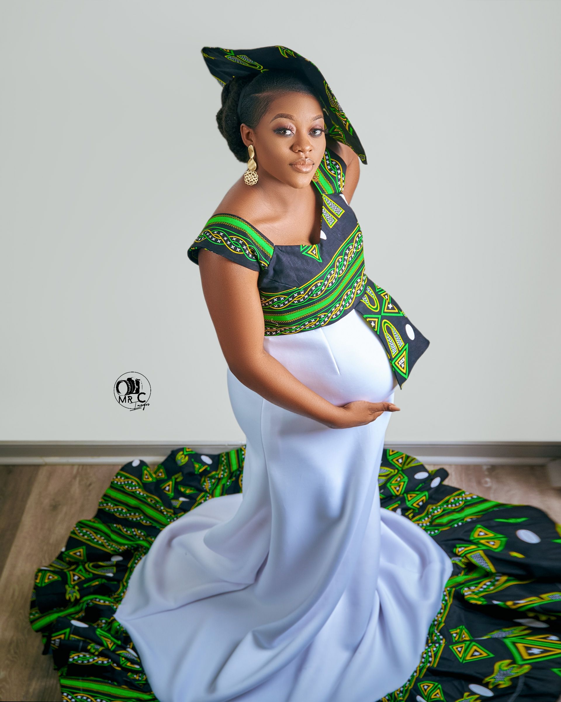 Elegant maternity portrait in white mermaid dress with green African print details and matching headwrap.