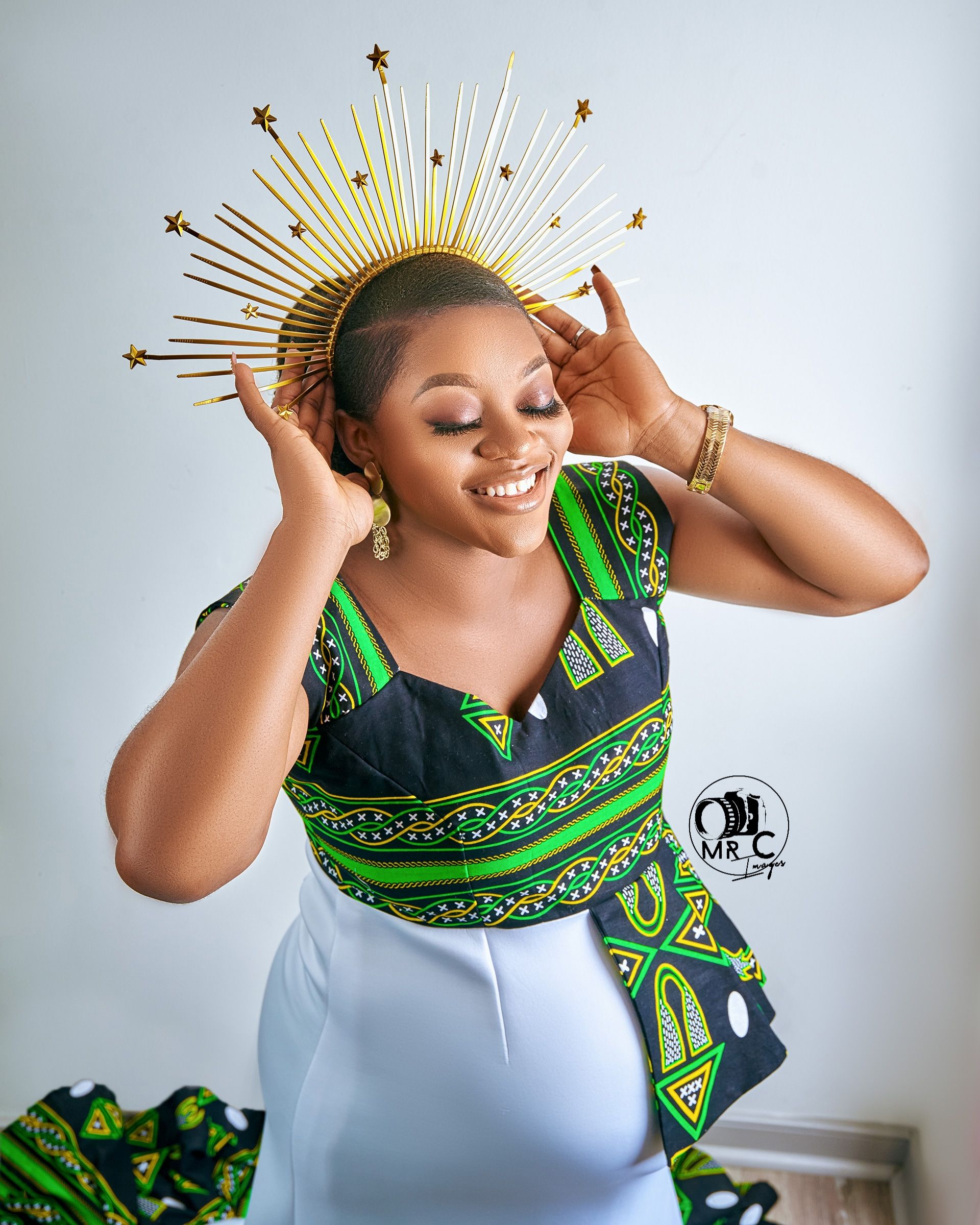 Studio portrait with golden sunburst crown and green African print dress details.