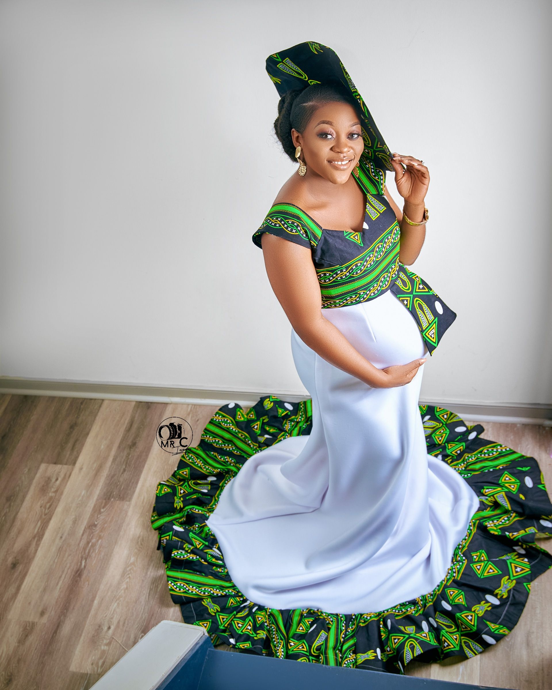 Maternity photo showcasing white gown with green African print details and matching headwrap.