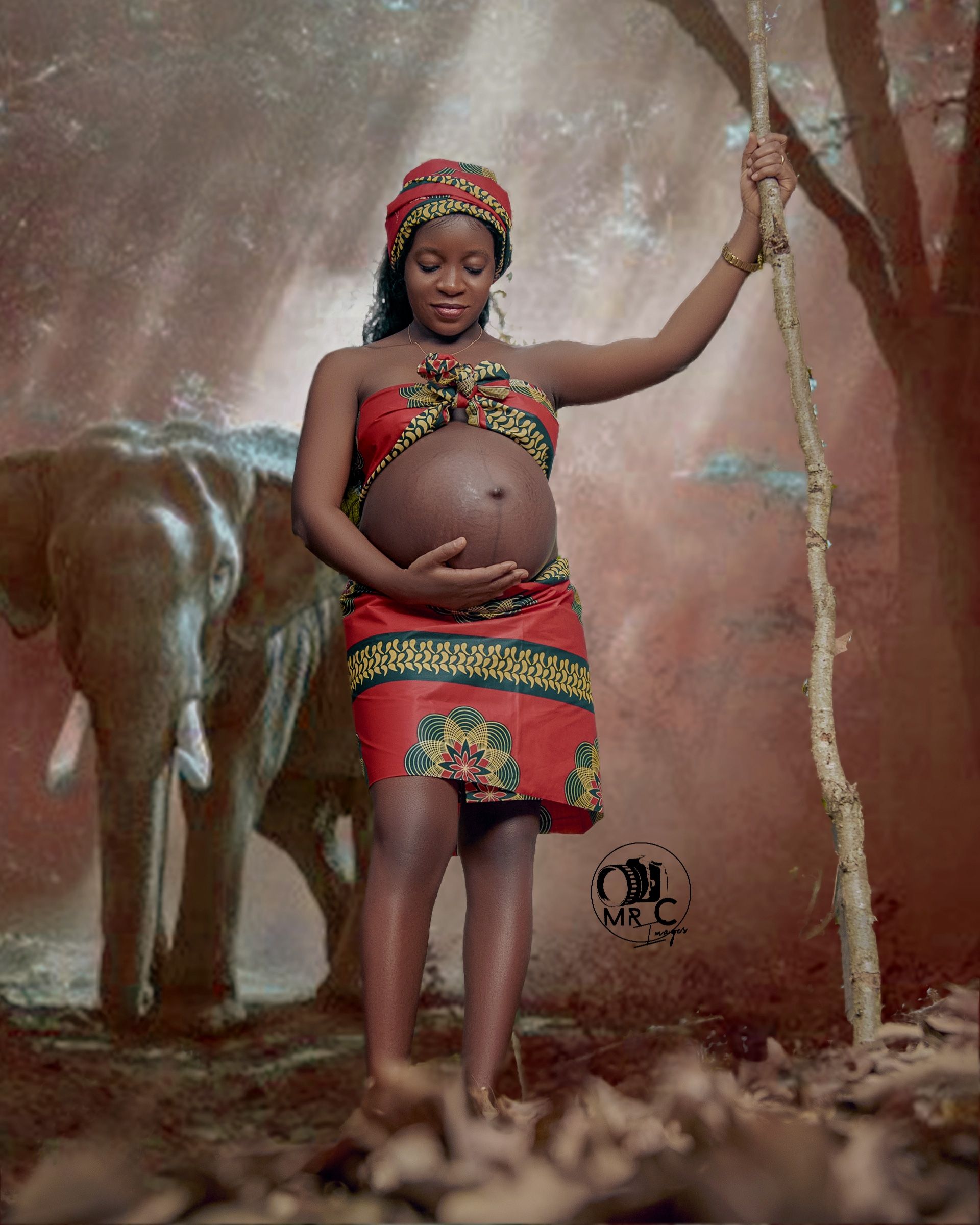 Artistic maternity portrait in traditional African attire with red and gold patterns in a misty forest setting.