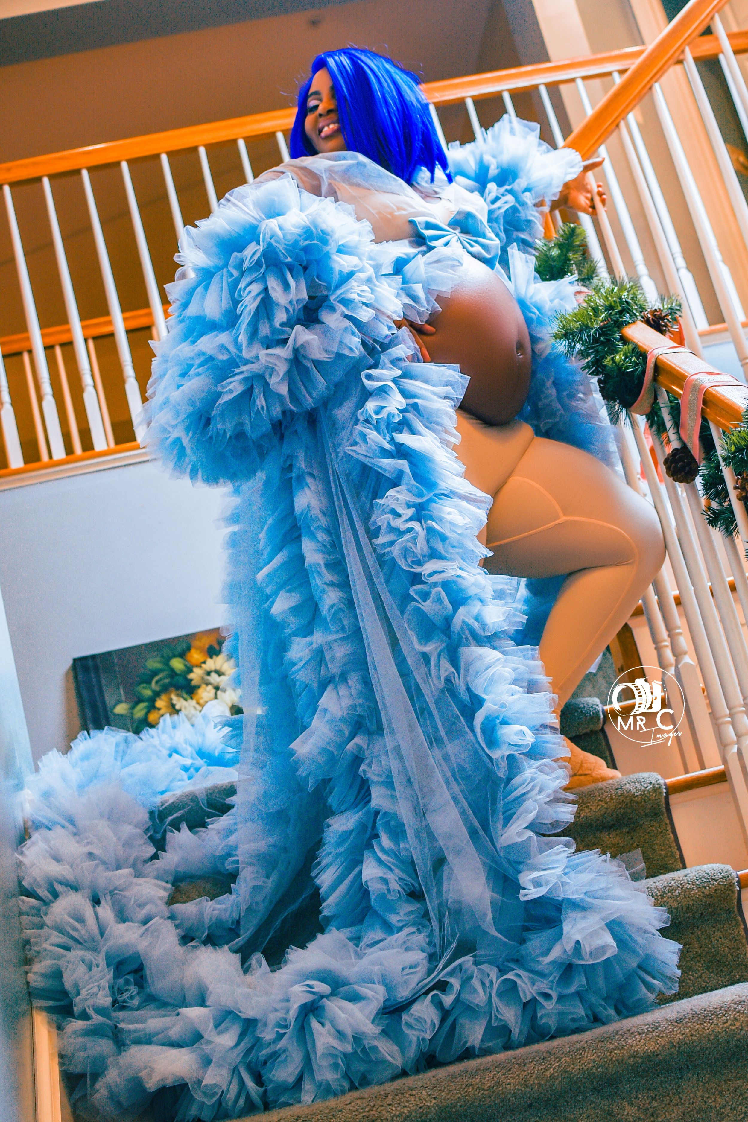 Dramatic maternity photo featuring flowing blue ruffled robe on carpeted stairs.