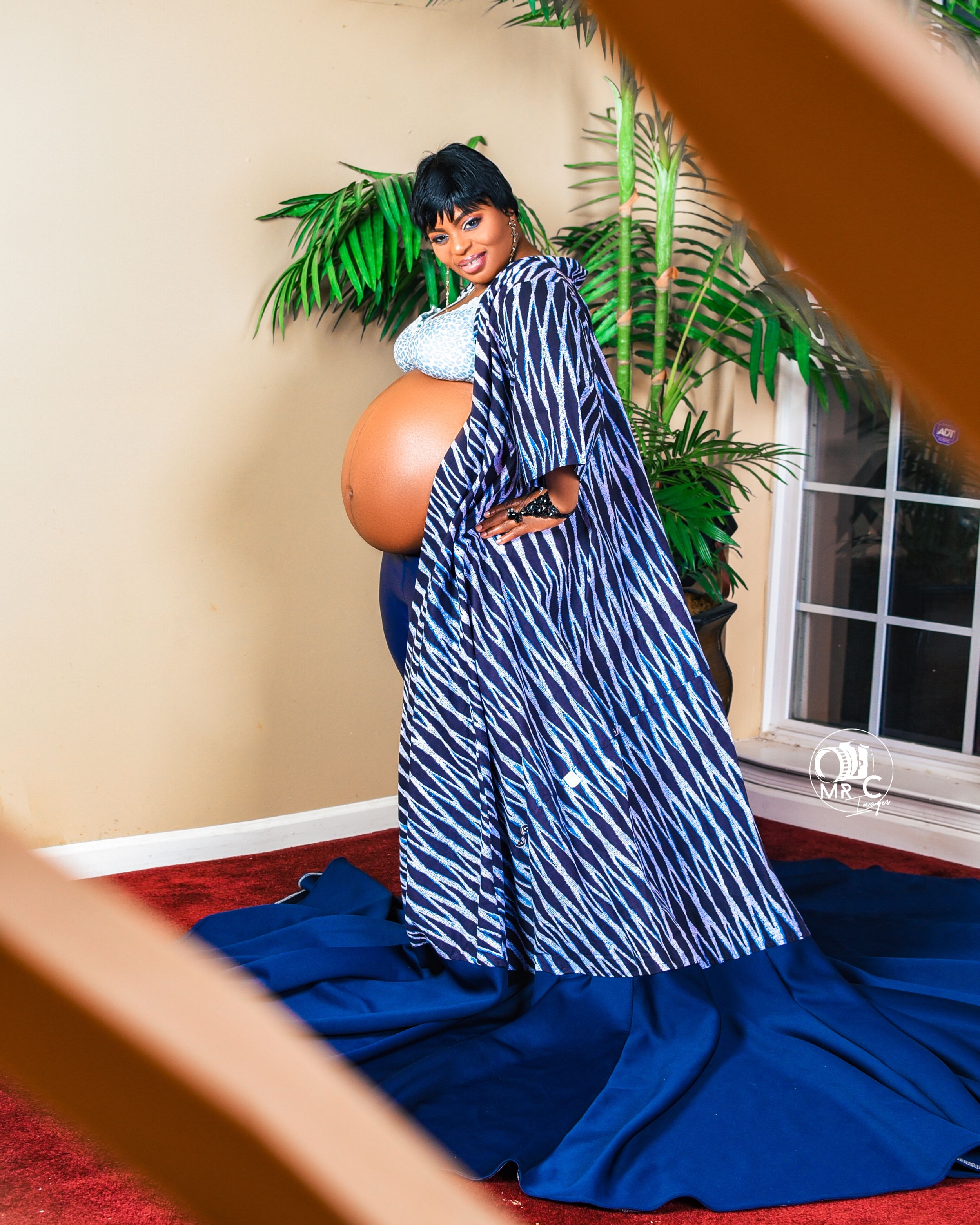 Maternity photoshoot with blue and white striped flowing dress against tropical palm backdrop.