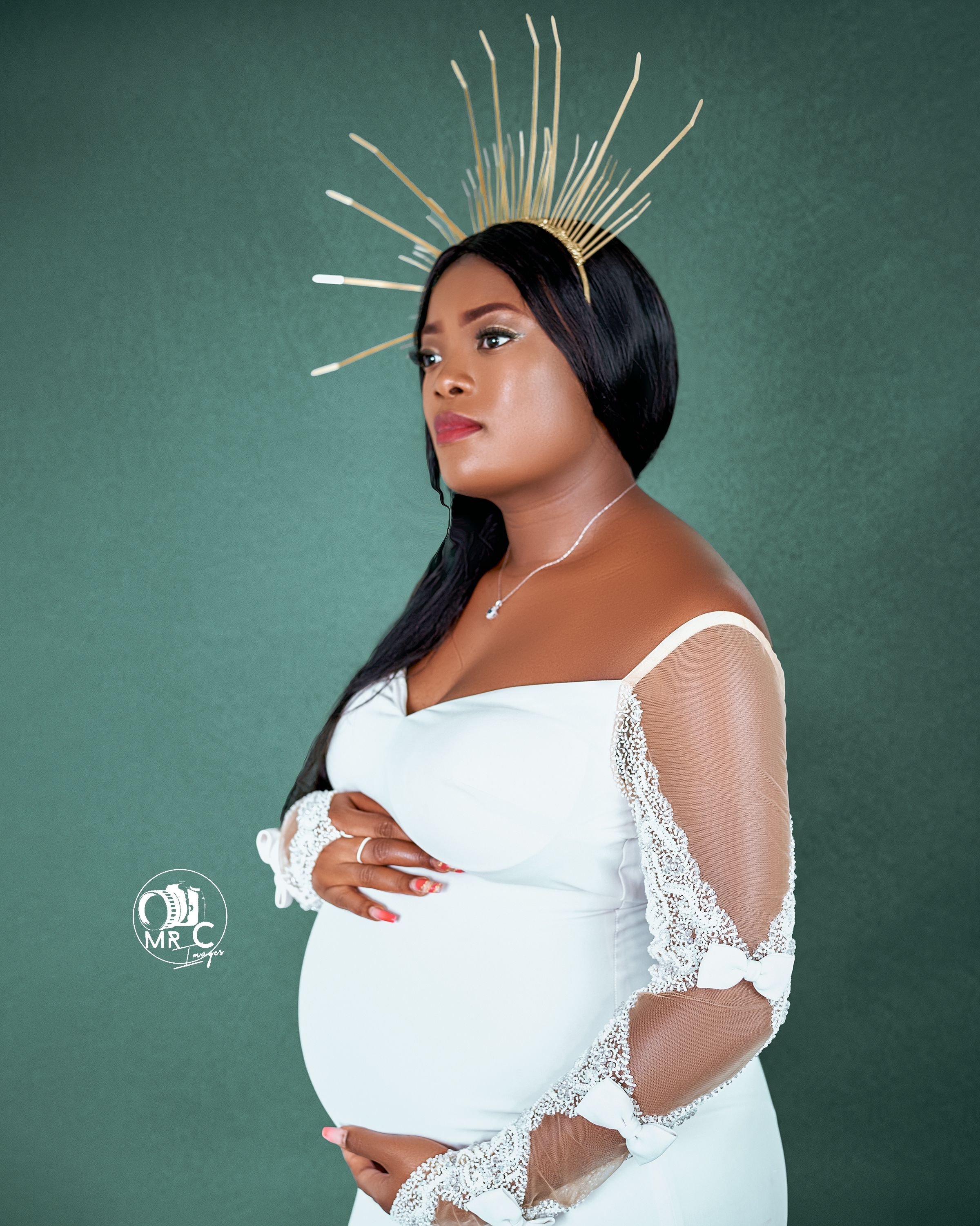 Maternity photo featuring a white lace dress and golden sunburst crown against a teal background.