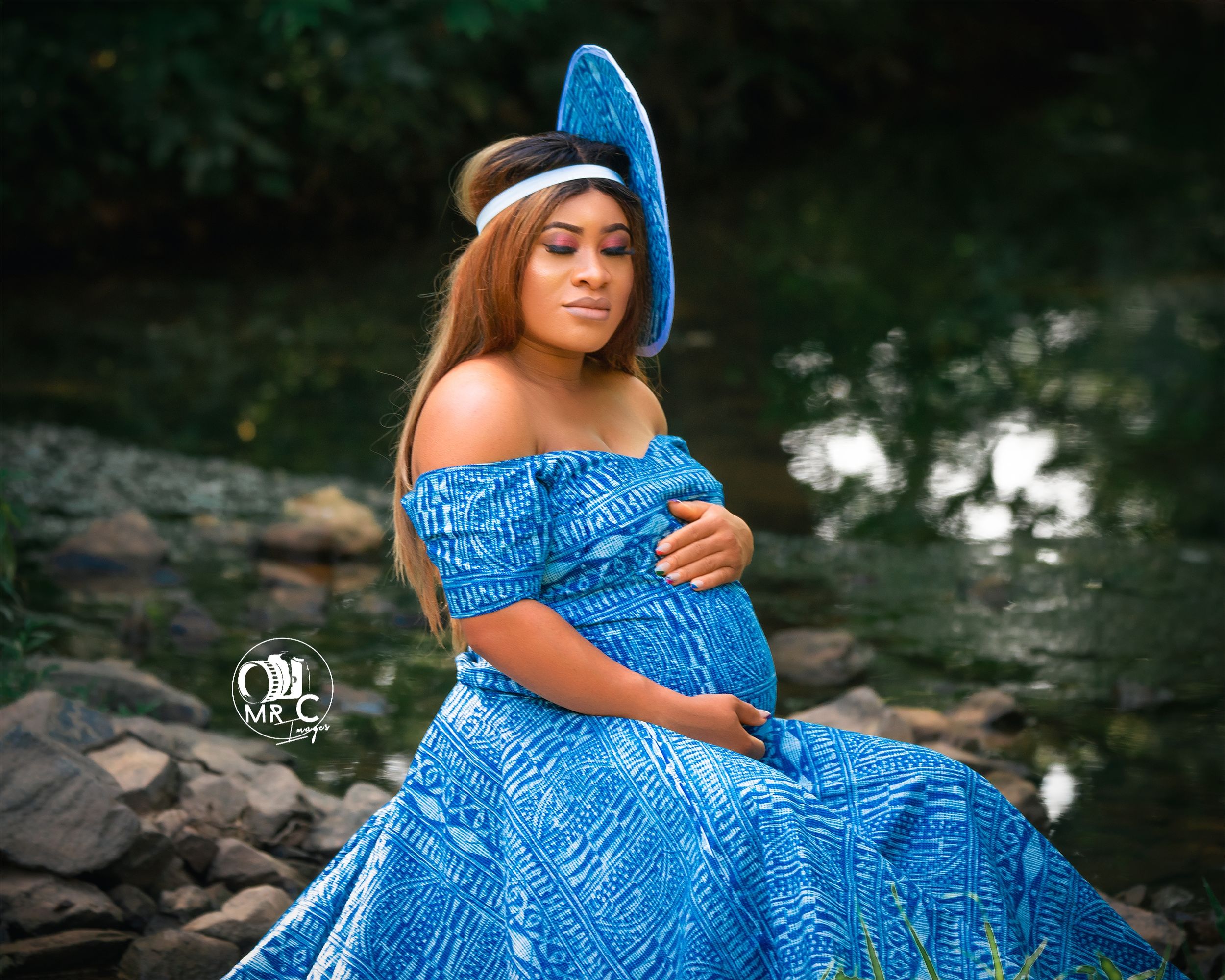 A blue sequined maternity gown with matching hat photographed by a rocky stream.