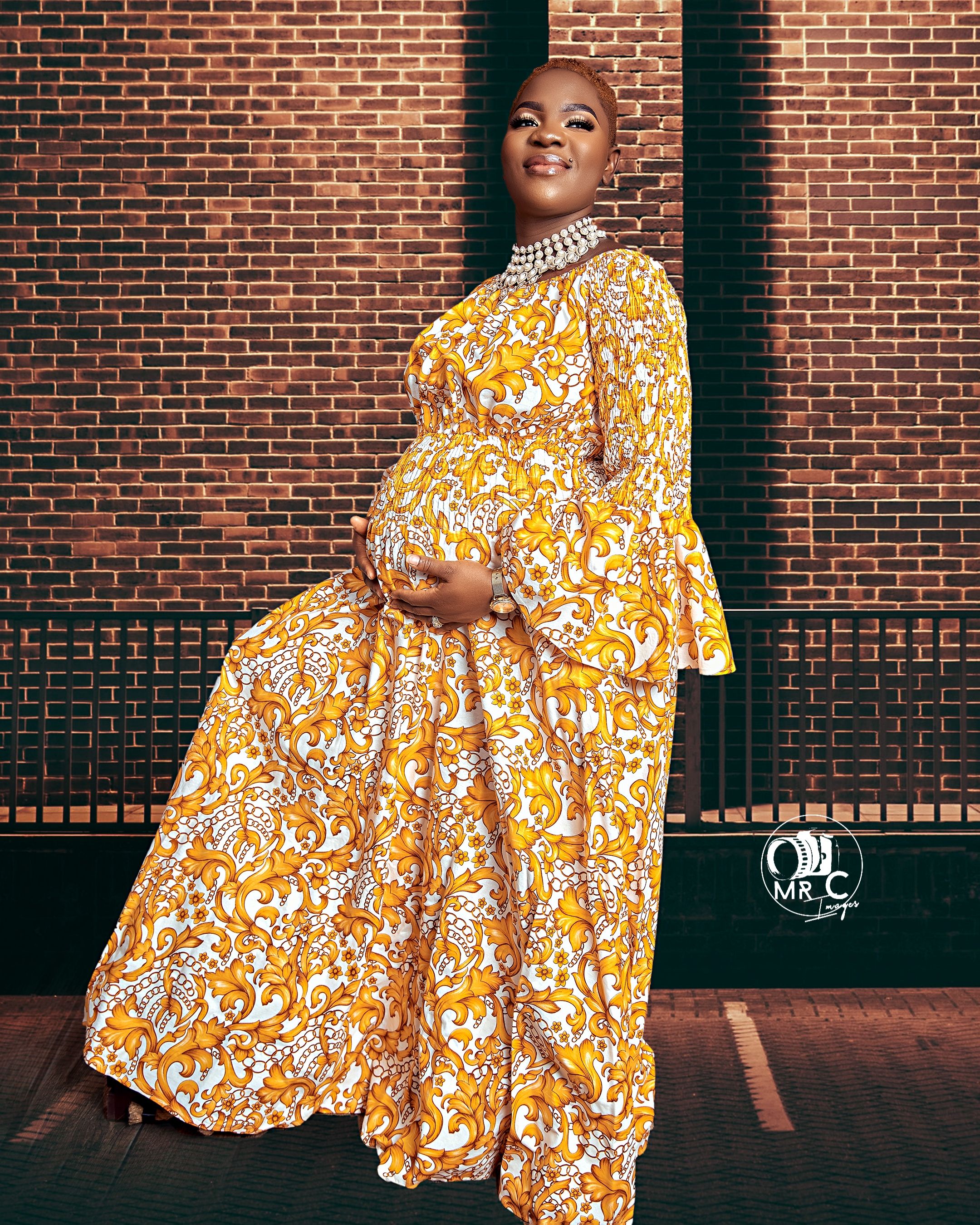 A flowing yellow and white floral print dress styled with a statement necklace against brick architecture.