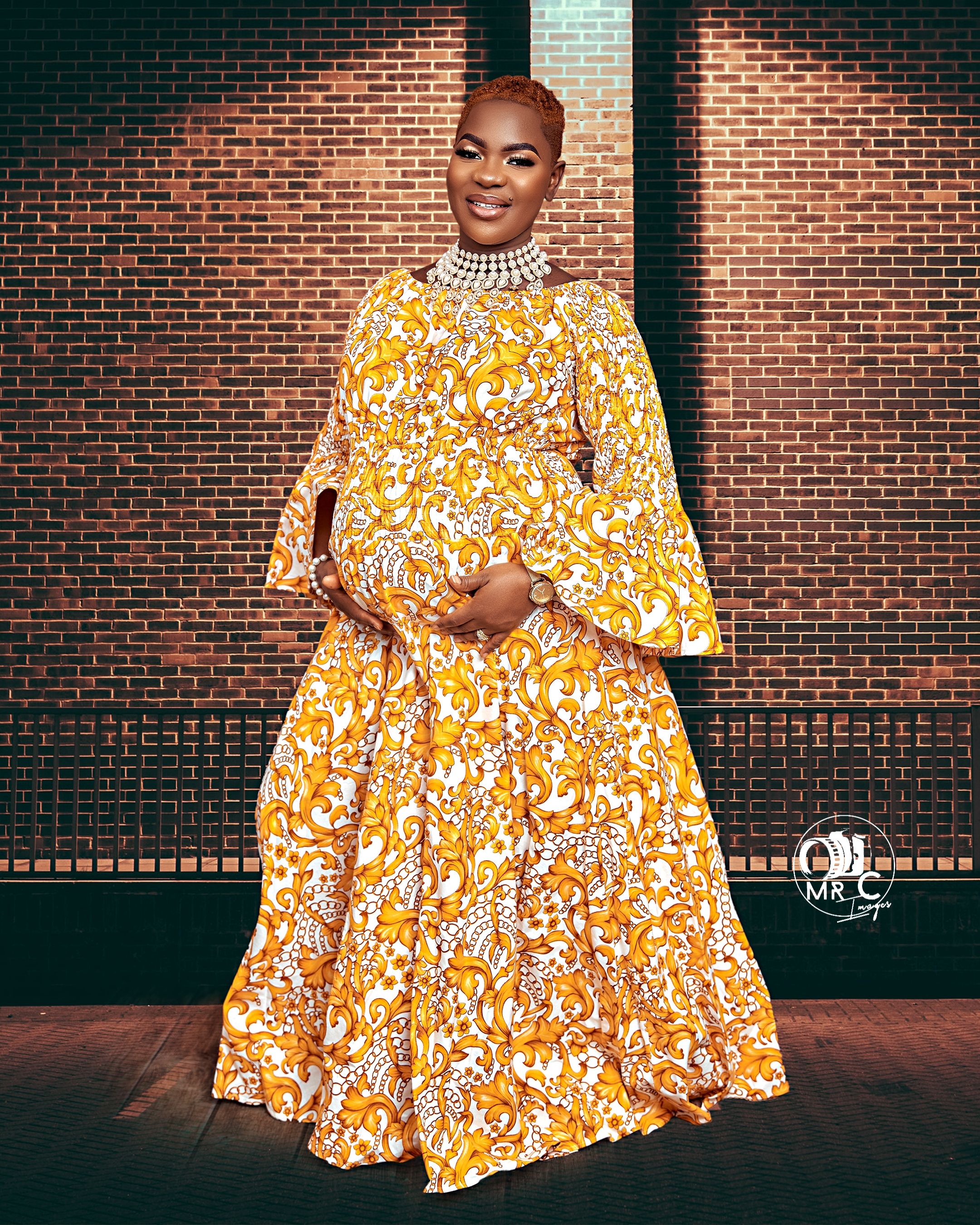 A vibrant yellow floral maxi dress with long sleeves photographed against a brick wall background.