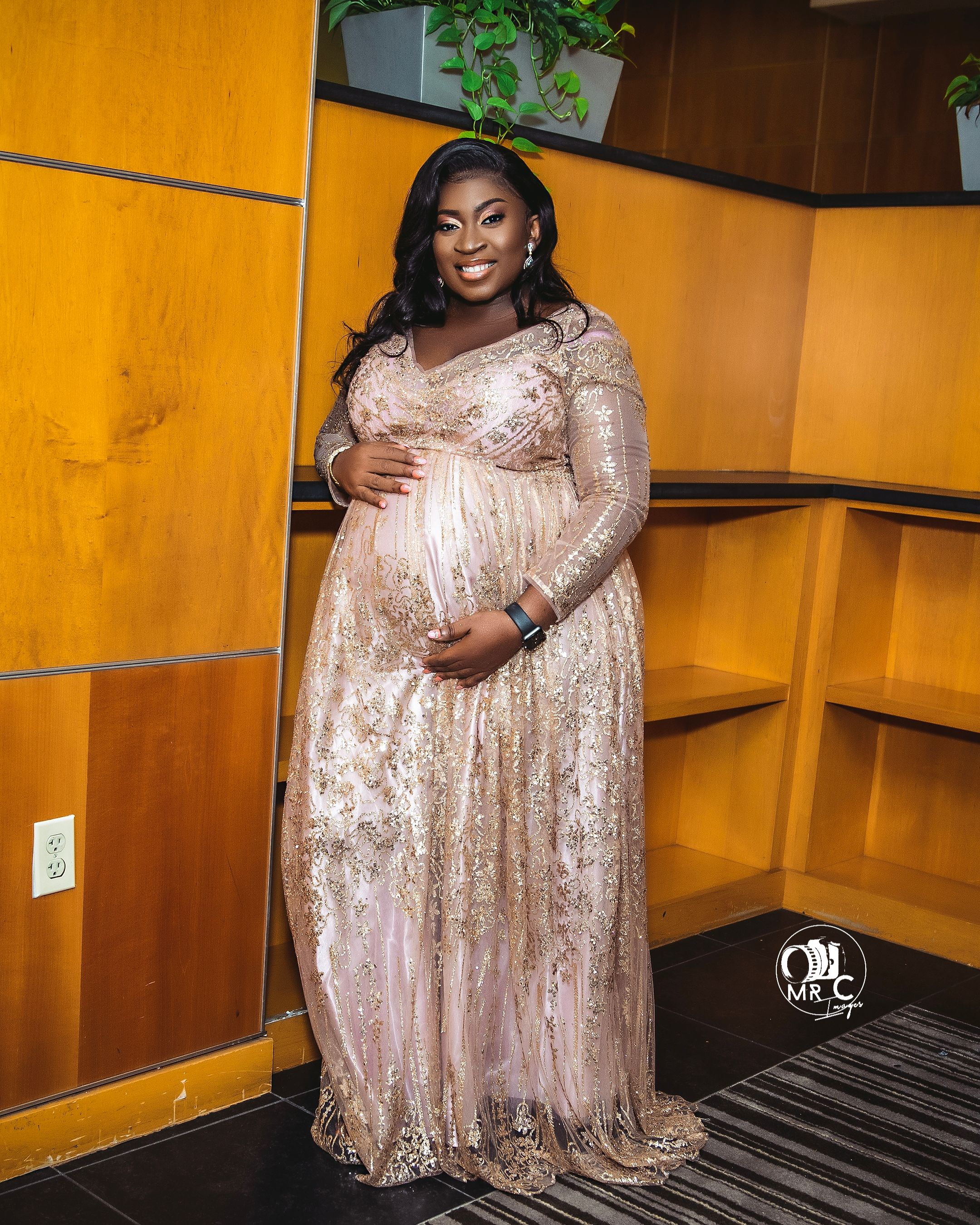 Elegant maternity portrait in sparkly champagne gown against warm orange-toned interior.
