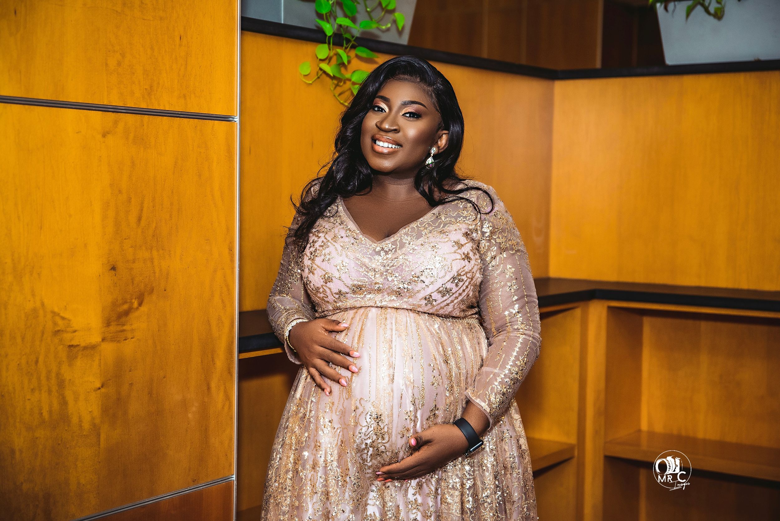 Maternity photo featuring sparkly champagne gown in warm-lit interior setting.