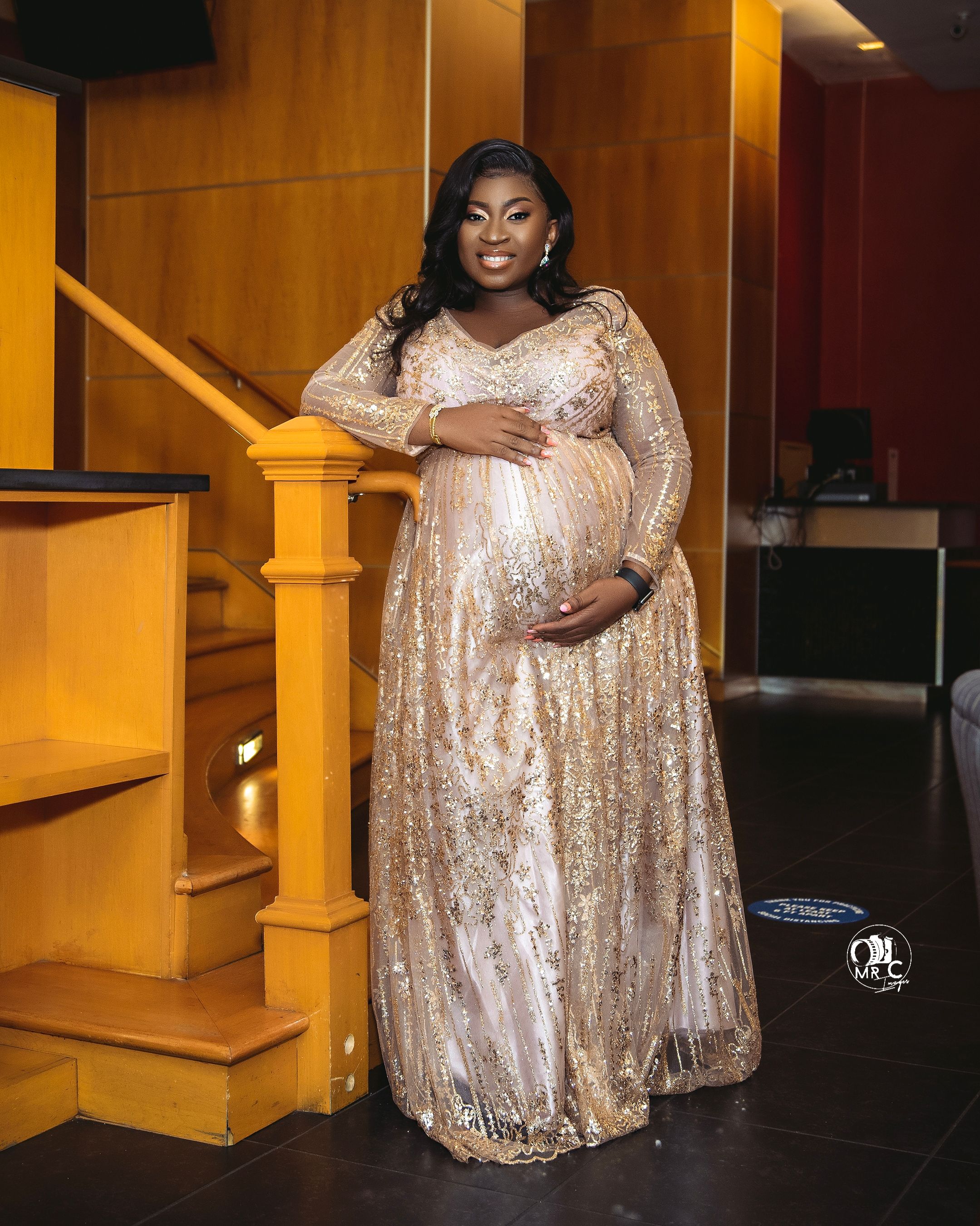 Glamorous maternity photo in champagne sequined gown against wooden interior backdrop.